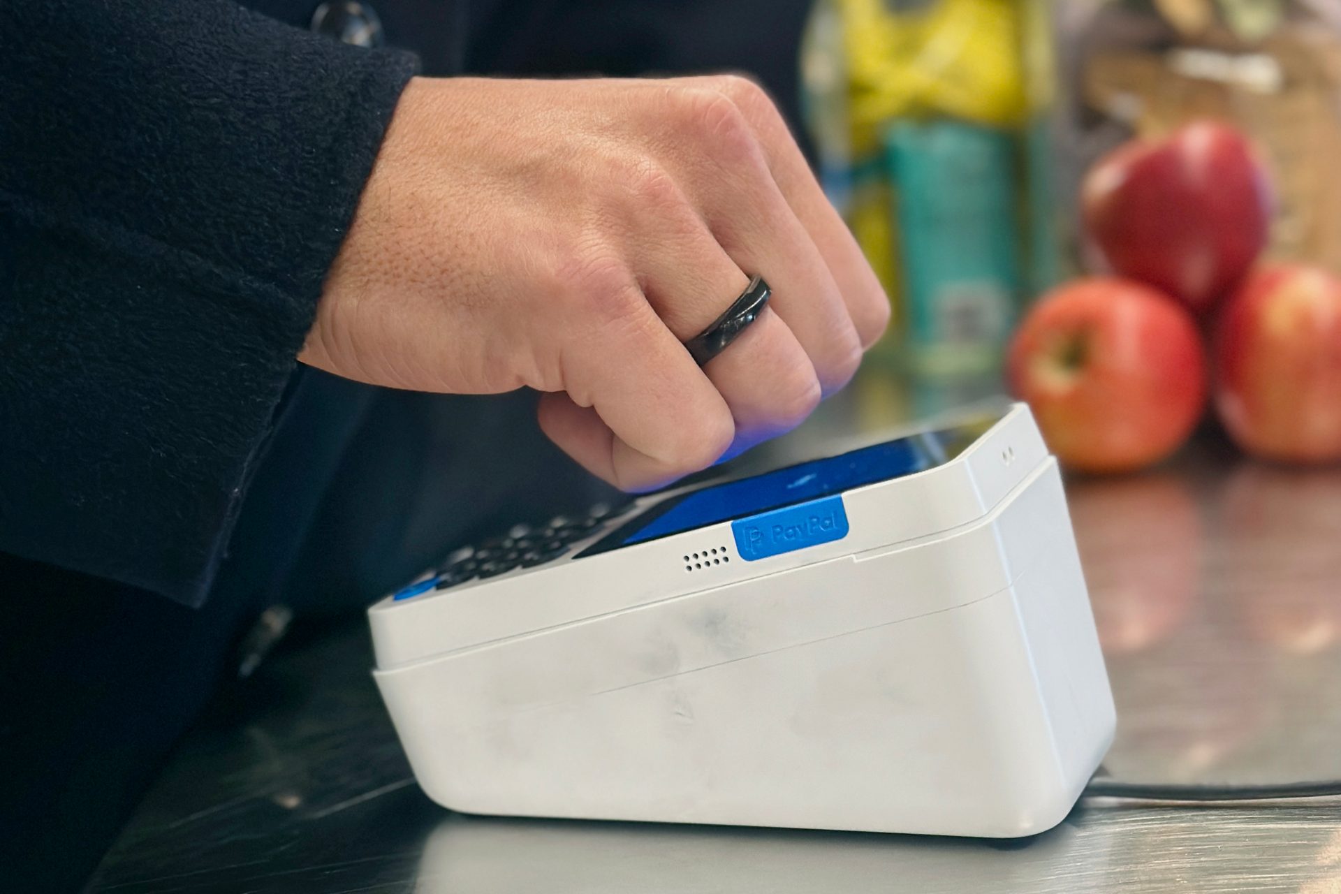 Hand with black ring tapping a PayPal payment terminal.