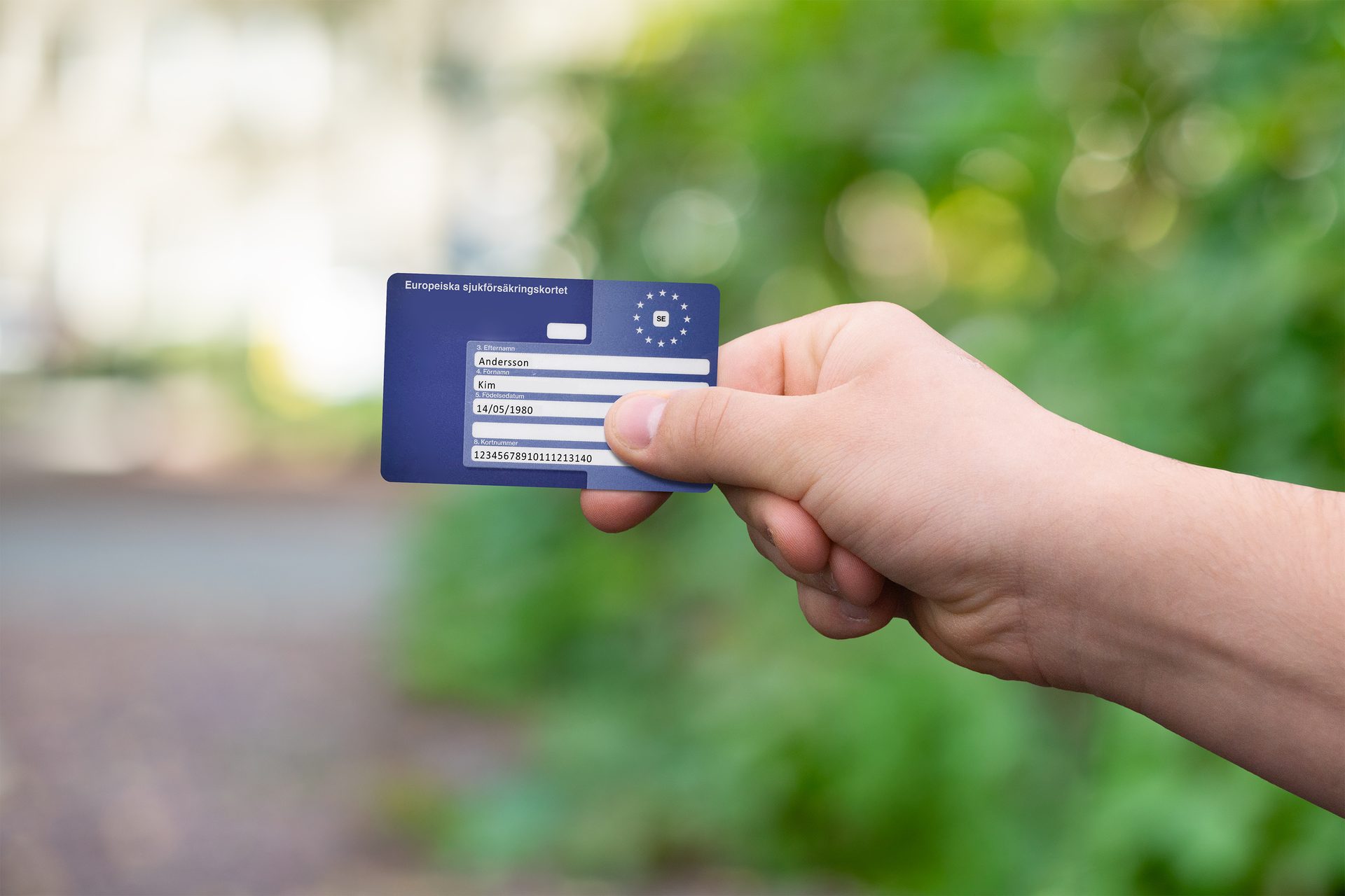 Hand holding a Swedish European Health Insurance Card against a blurred green background.