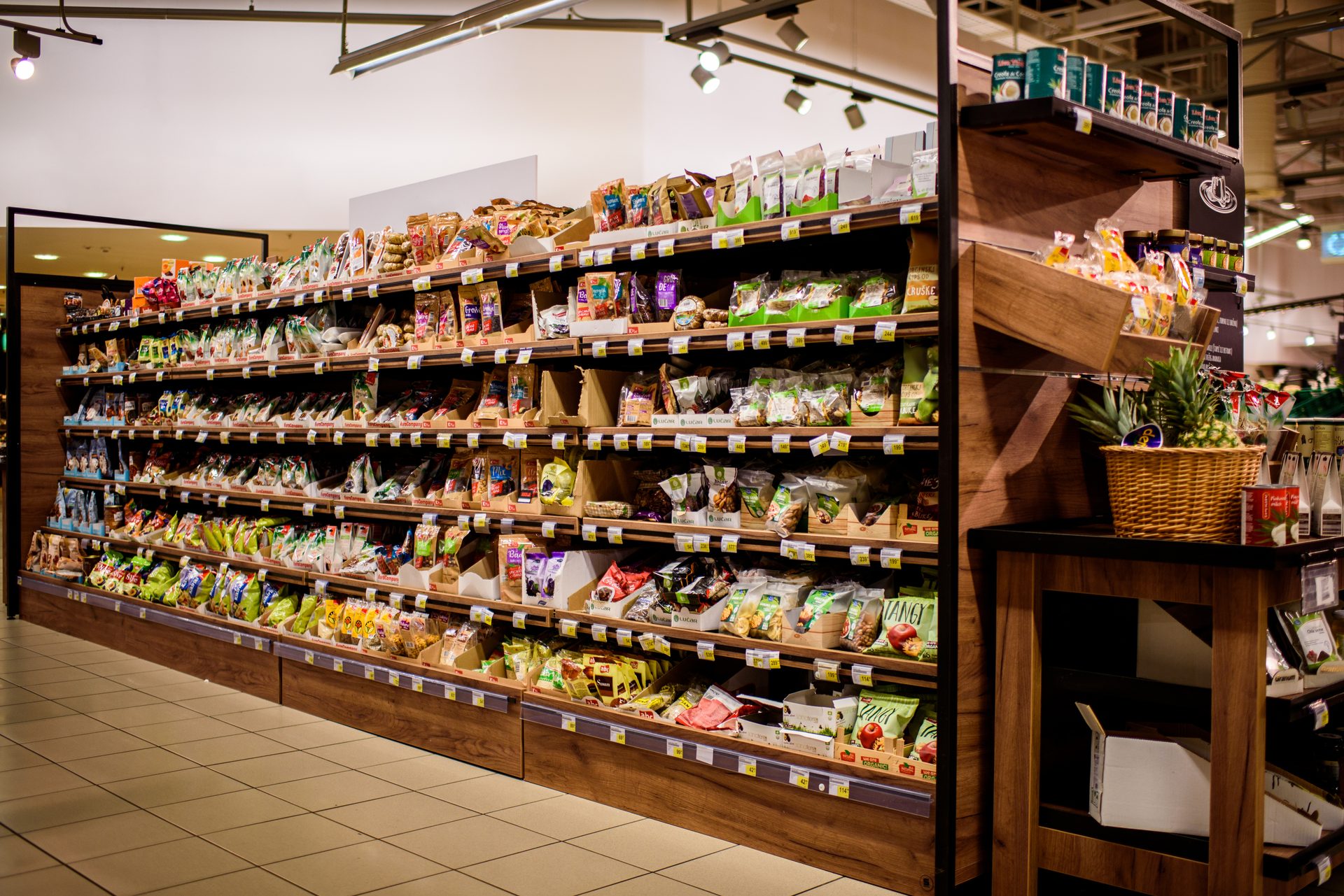 Supermarket aisle with long shelves of packaged snacks and goods, and a side display with pineapples.