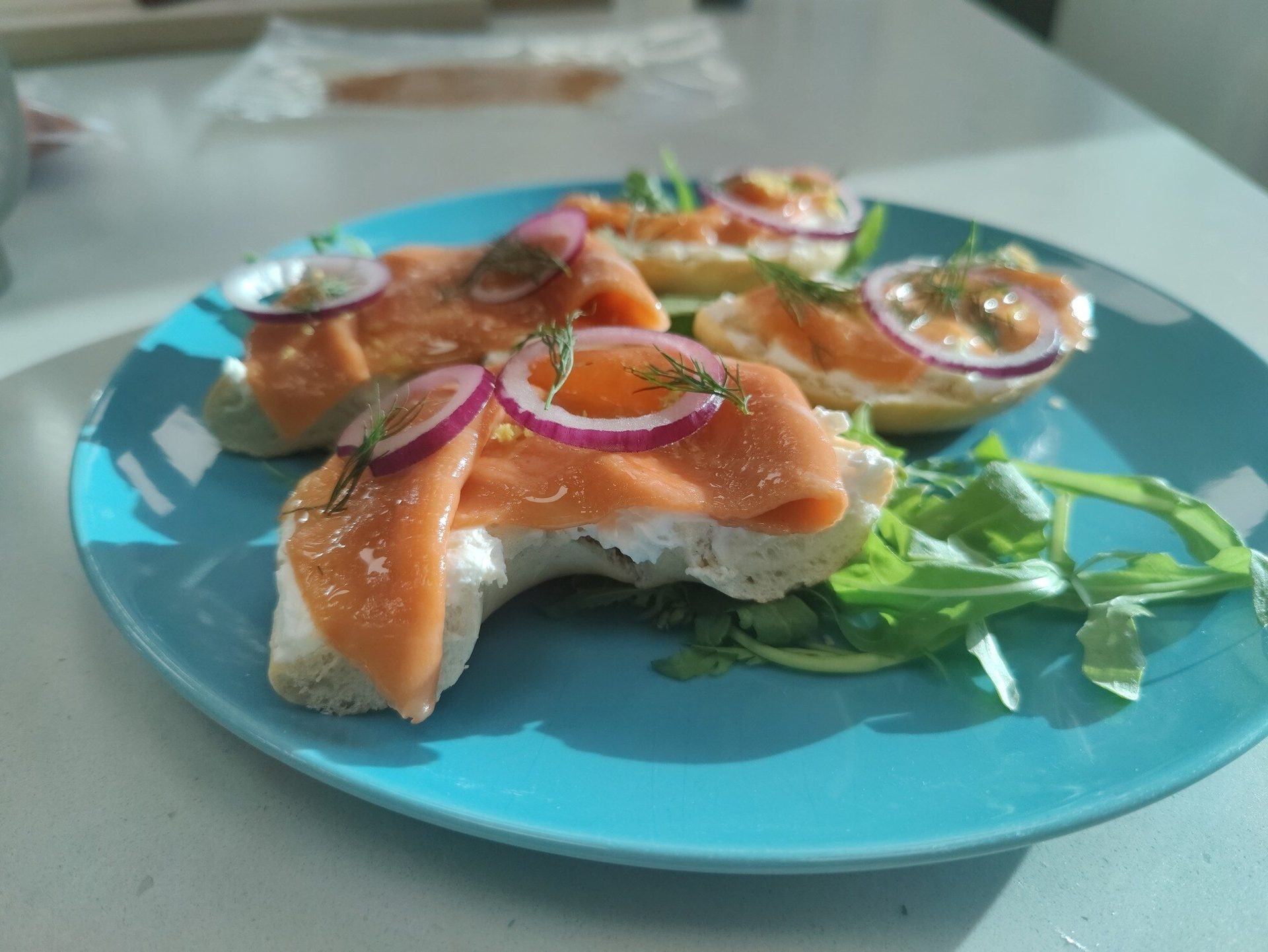 Smoked salmon and cream cheese appetizers with red onion, dill, and arugula on a blue plate.