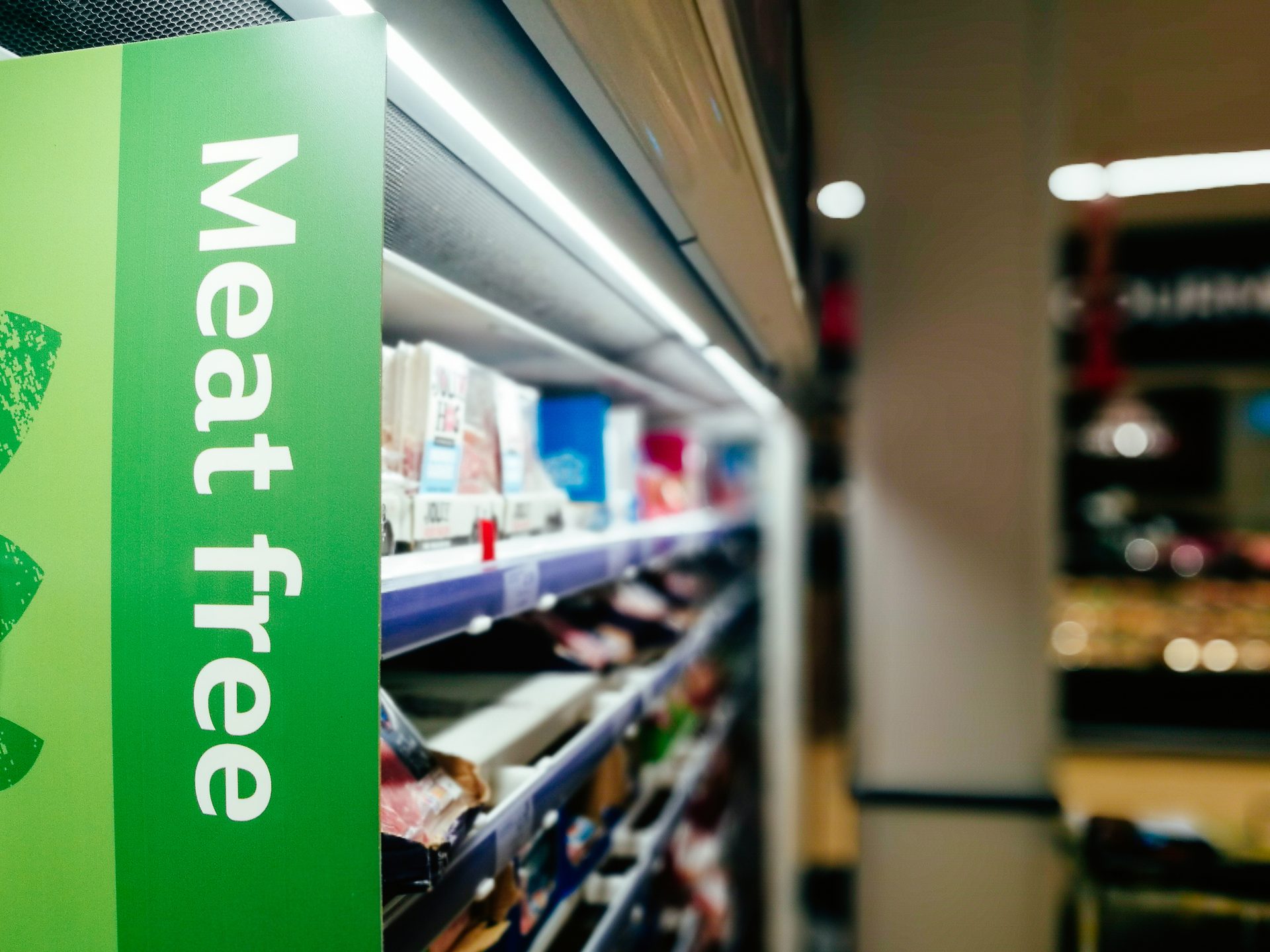 Green "Meat Free" sign in a supermarket aisle, with blurred product shelves.