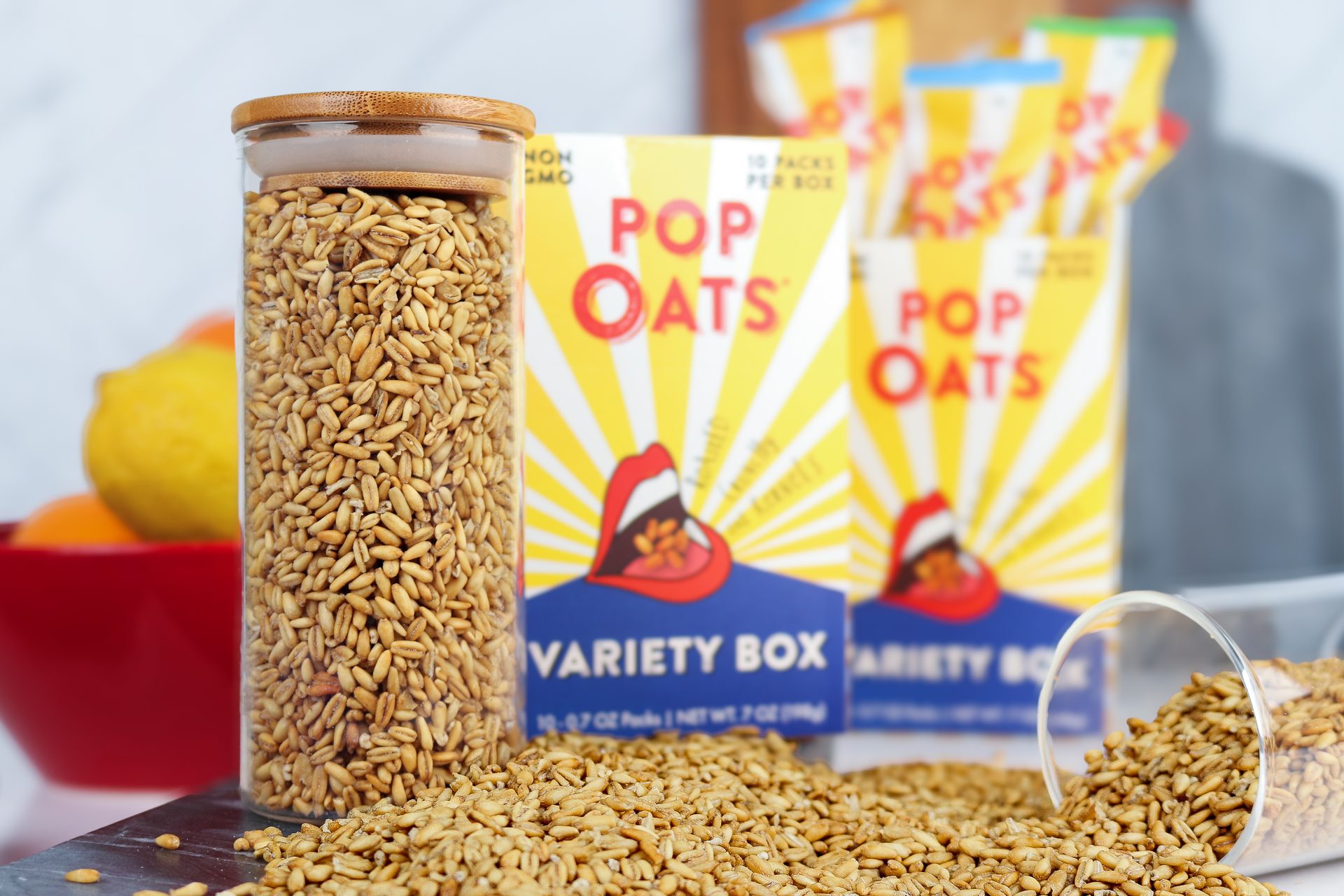 Oats in a jar and spilled, with "POP OATS" boxes and fruit blurred in the background.
