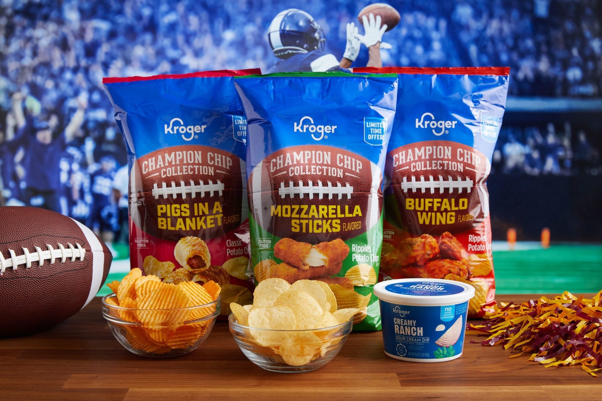 Three Kroger Champion Chip Collection bags (Pigs in a Blanket, Mozzarella Sticks, Buffalo Wing) with chips, ranch dip, and a football on a table for game day.