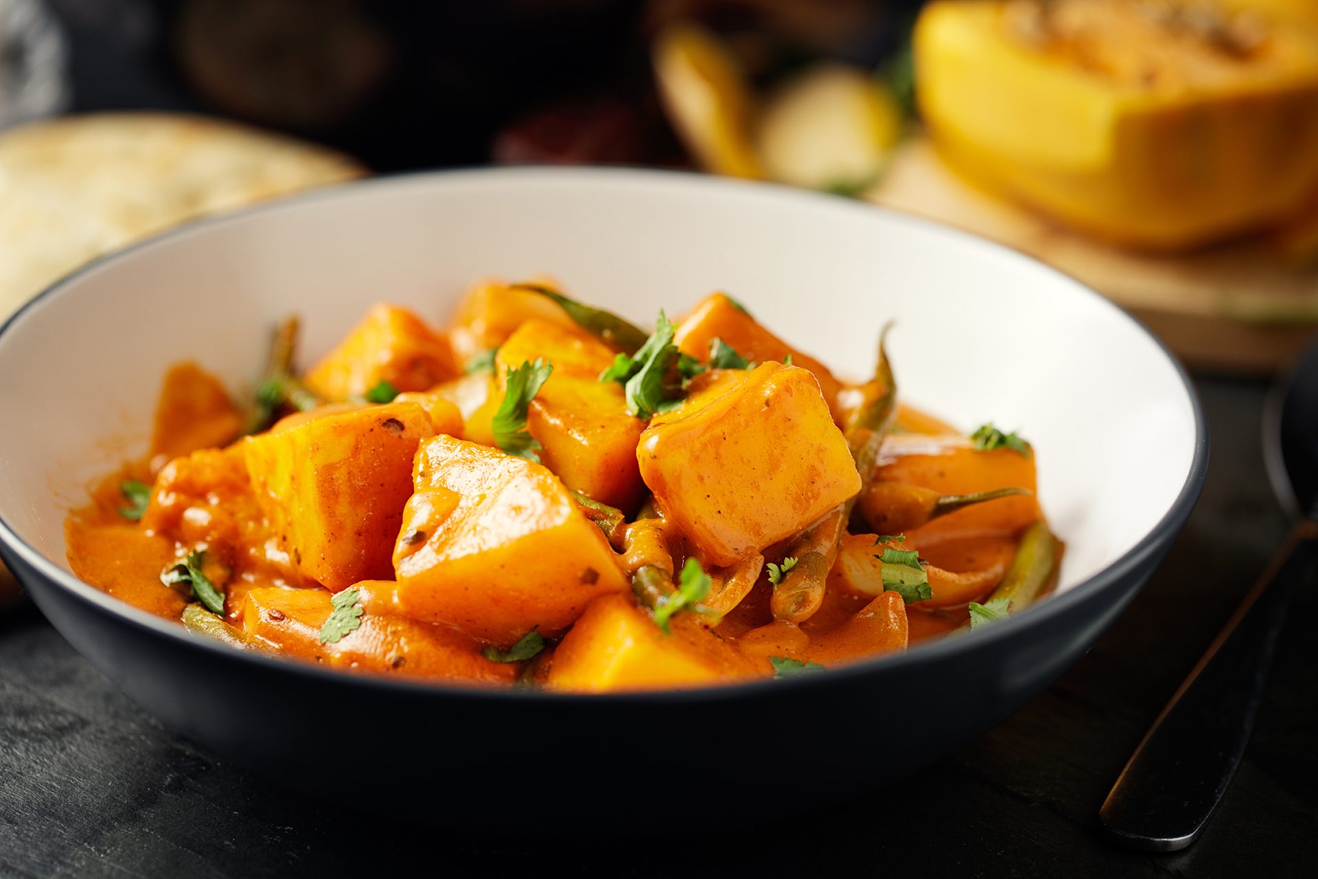A bowl of vibrant orange pumpkin curry with green herbs.