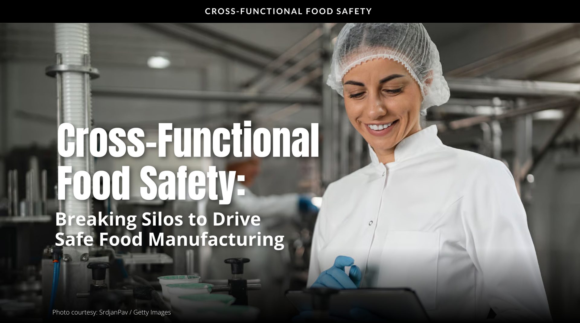 A smiling woman in a lab coat and hairnet, working in a food processing plant.
