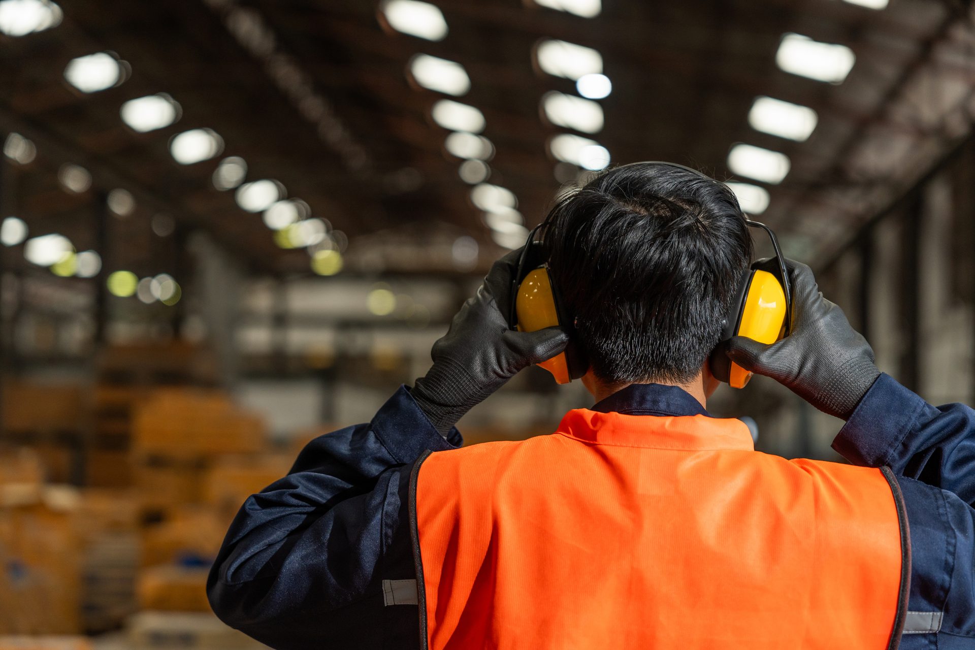 Worker from behind putting on yellow ear protection in a warehouse.