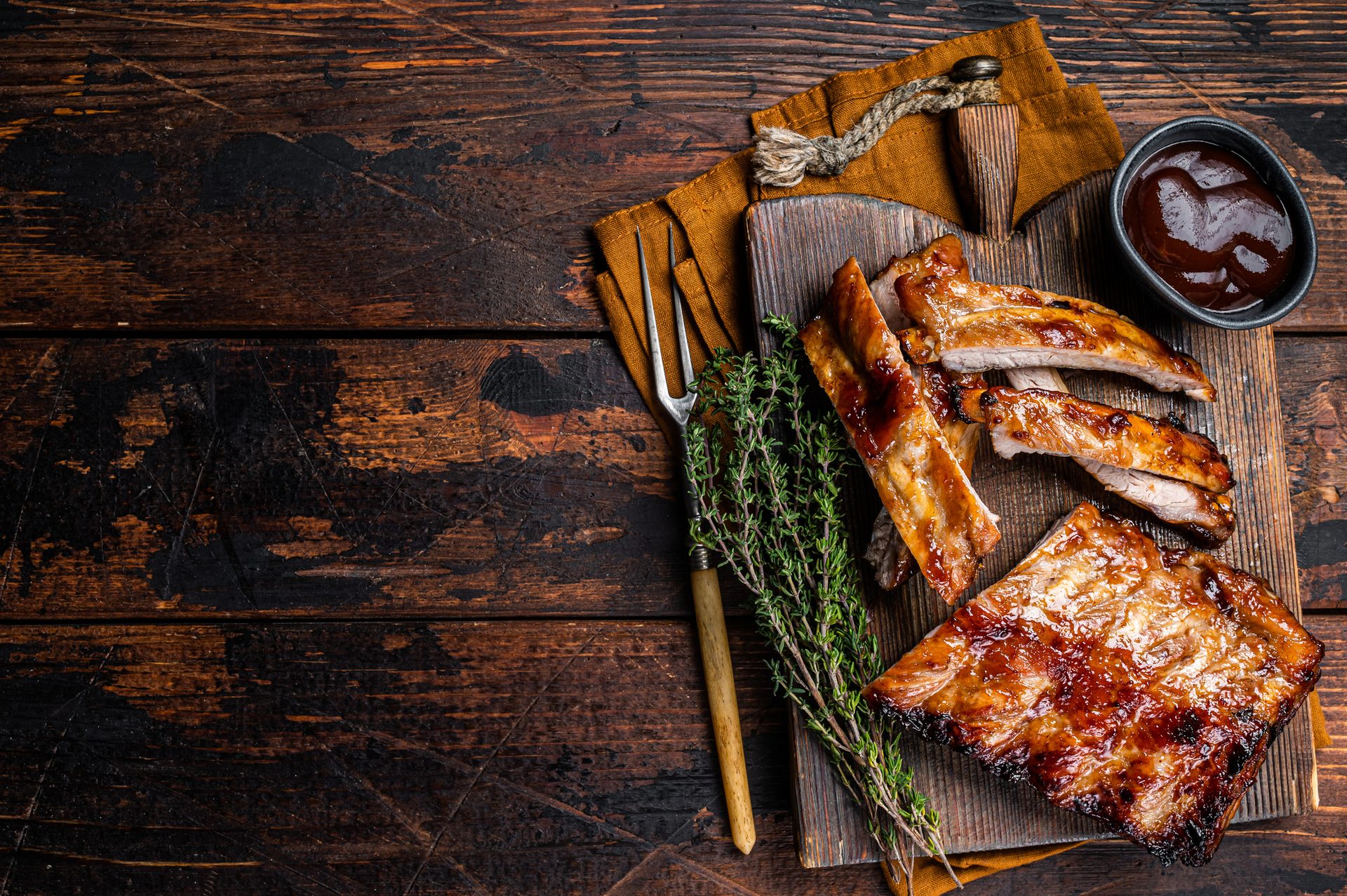 Glazed pork ribs with BBQ sauce and thyme on a dark wooden table.