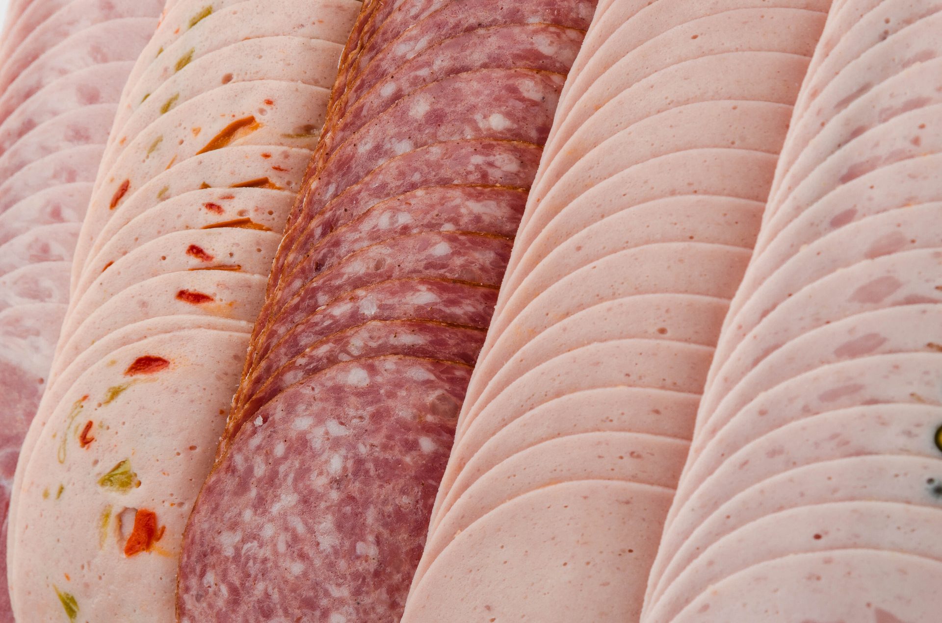 Close-up of rows of various sliced deli meats including ham, salami, and peppered turkey.