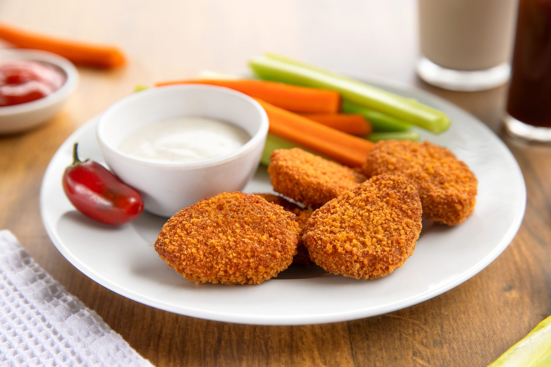 Golden nuggets, carrot and celery sticks, and two dips on a white plate with a red pepper.