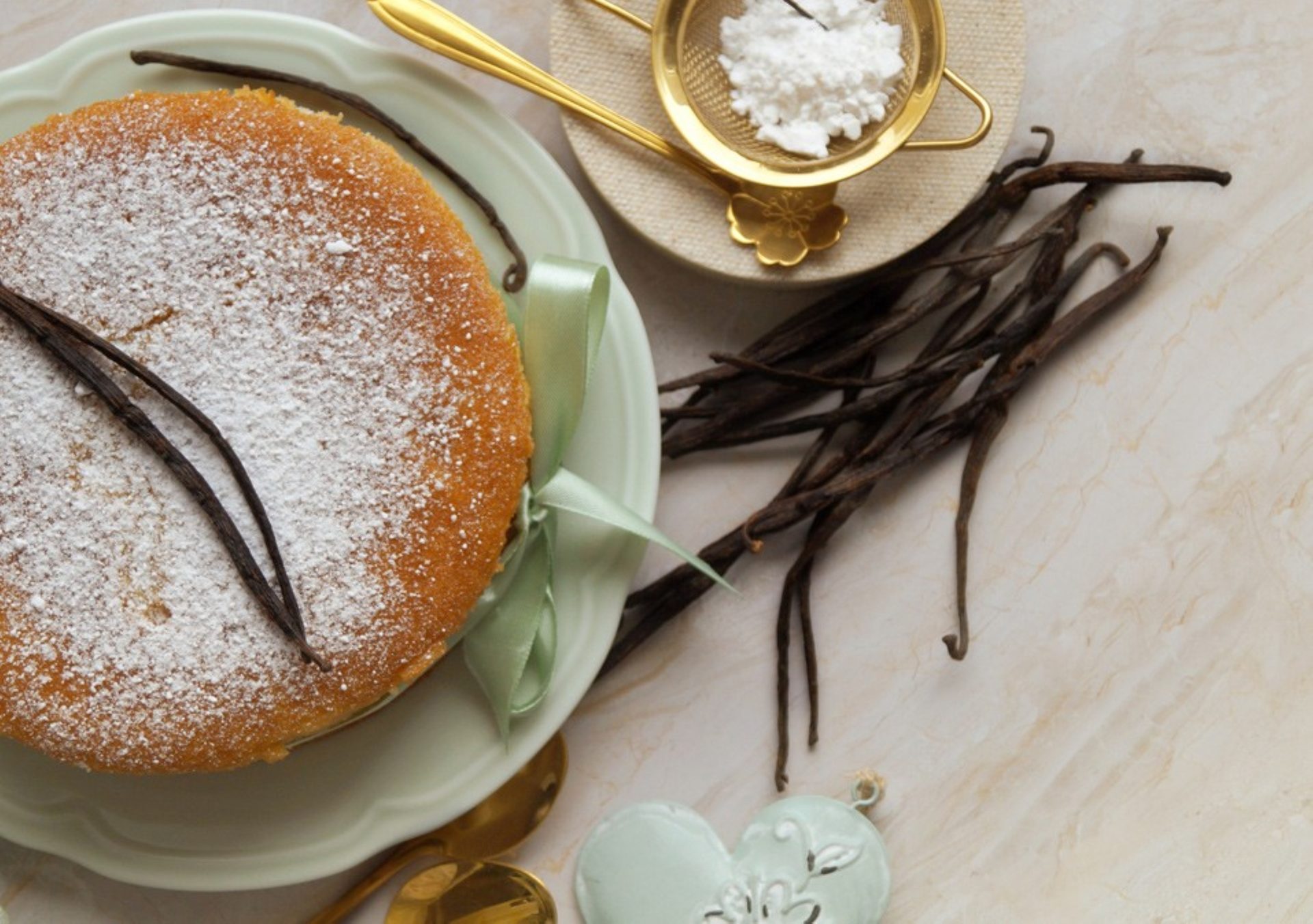 Vanilla cake with powdered sugar and vanilla pods, alongside a sieve of powdered sugar.