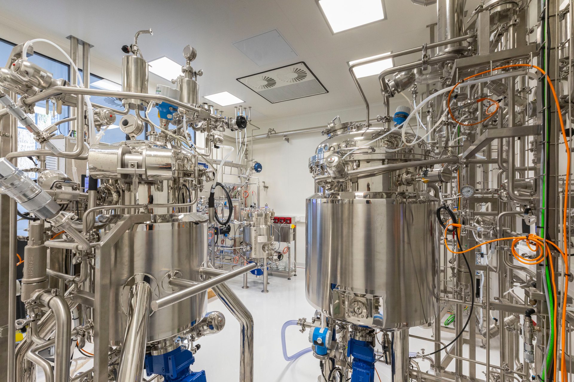 A modern biopharmaceutical cleanroom with two large stainless steel bioreactors and intricate piping.