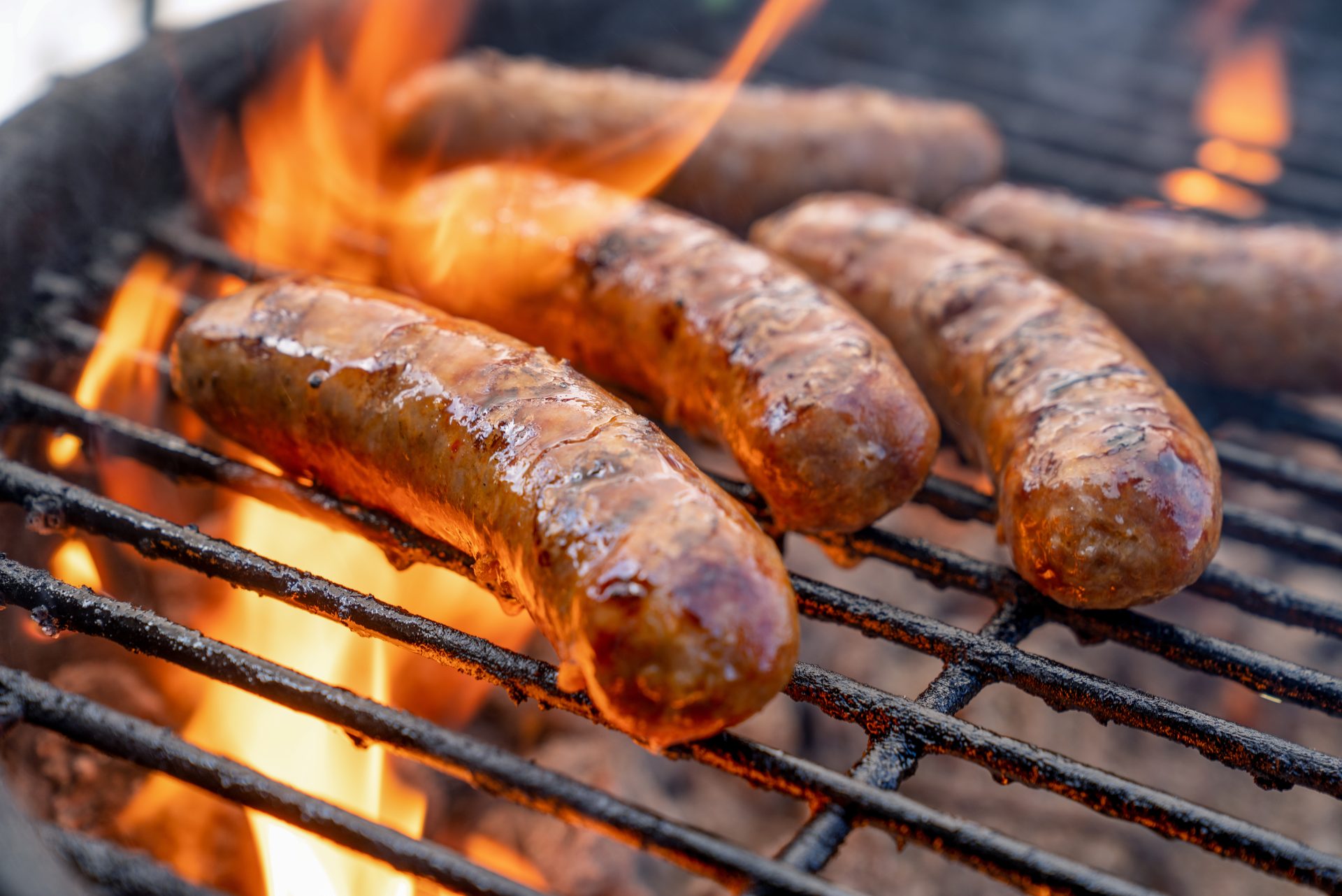 Sausages grilling over open flames, sizzling and browning on a barbecue.