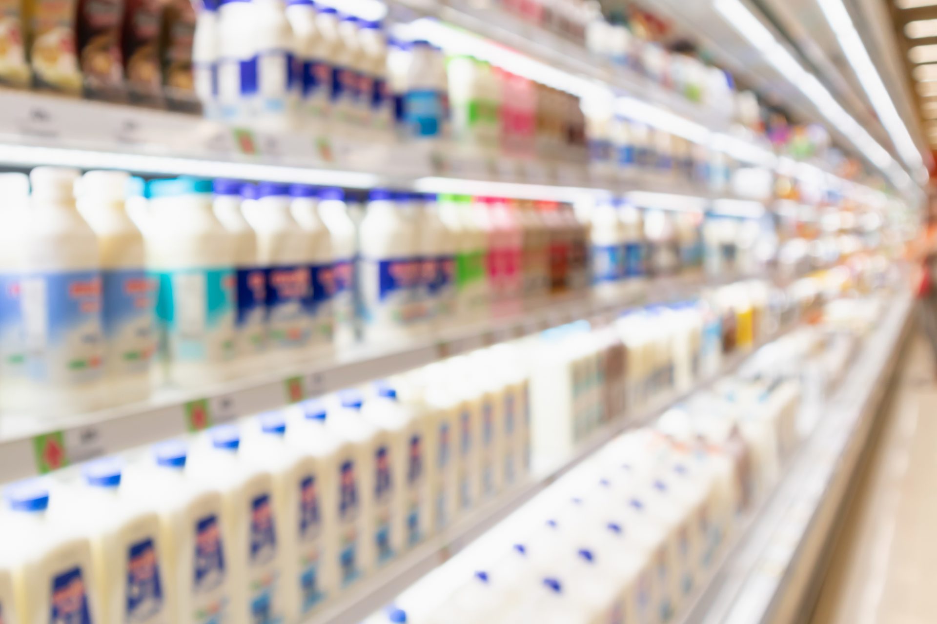 Blurred supermarket aisle with milk bottles and cartons on illuminated shelves.