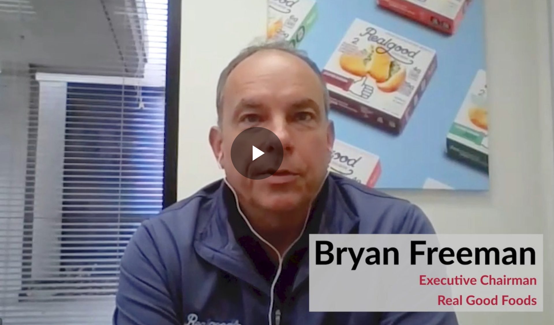 Bryan Freeman, Executive Chairman of Real Good Foods, on a video call with product poster in background.