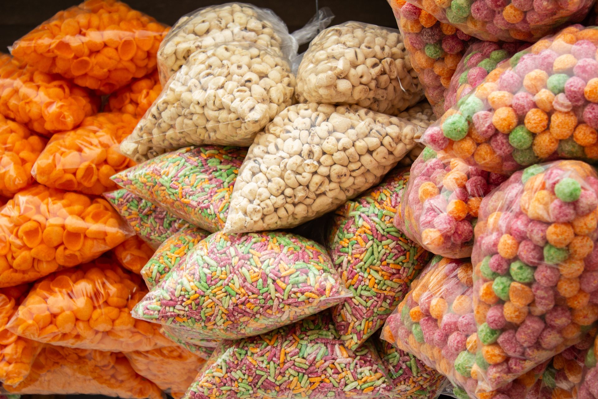 Bags of assorted colorful Indian snacks: orange shells, white puffs, sprinkles, and colorful balls.