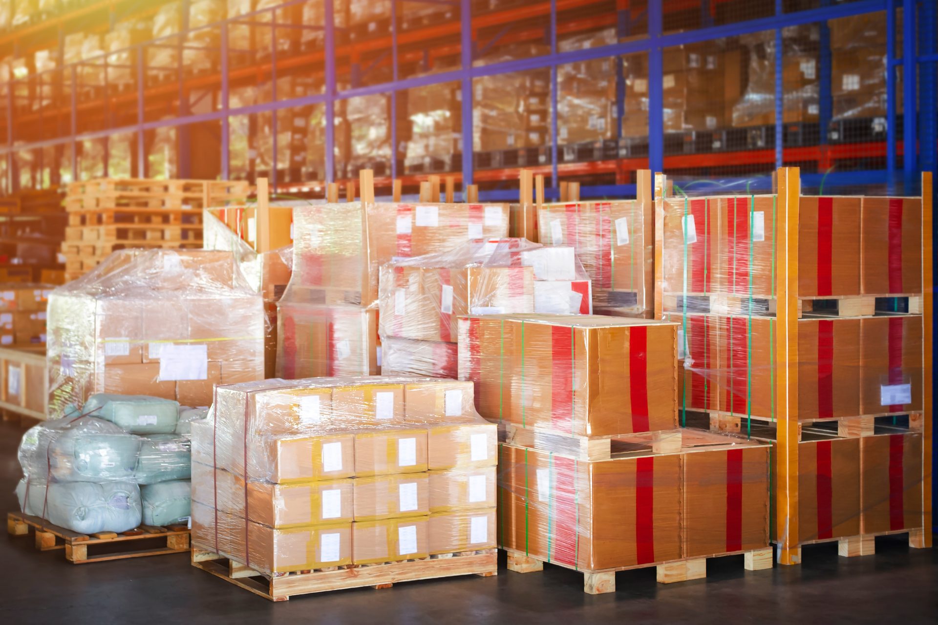 Pallets of various packaged goods, including boxes and bags, stacked high in a busy warehouse setting.