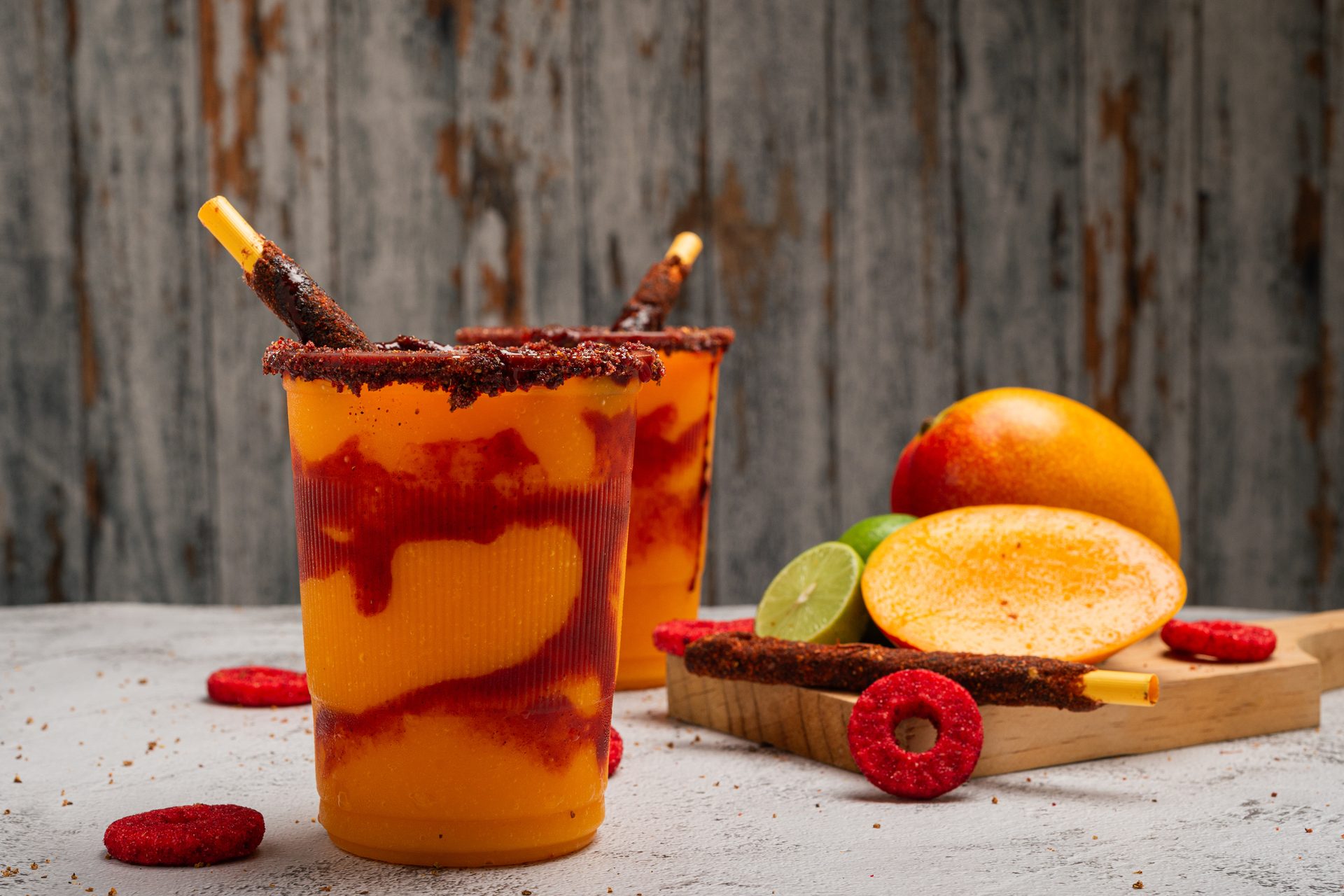 Spicy mango drinks with chili-dusted rims and tamarind candy straws, alongside fresh mango and lime.