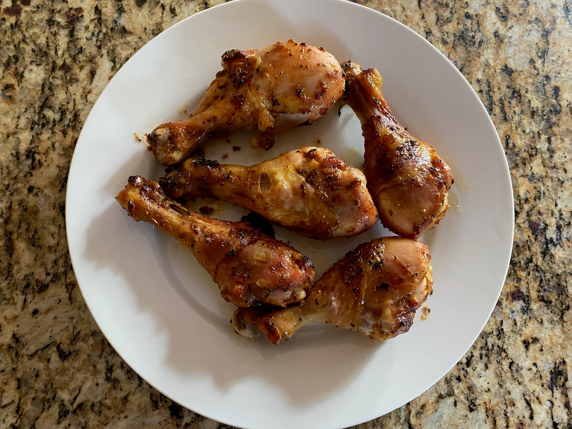 Five glossy, golden-brown chicken drumsticks on a white plate.