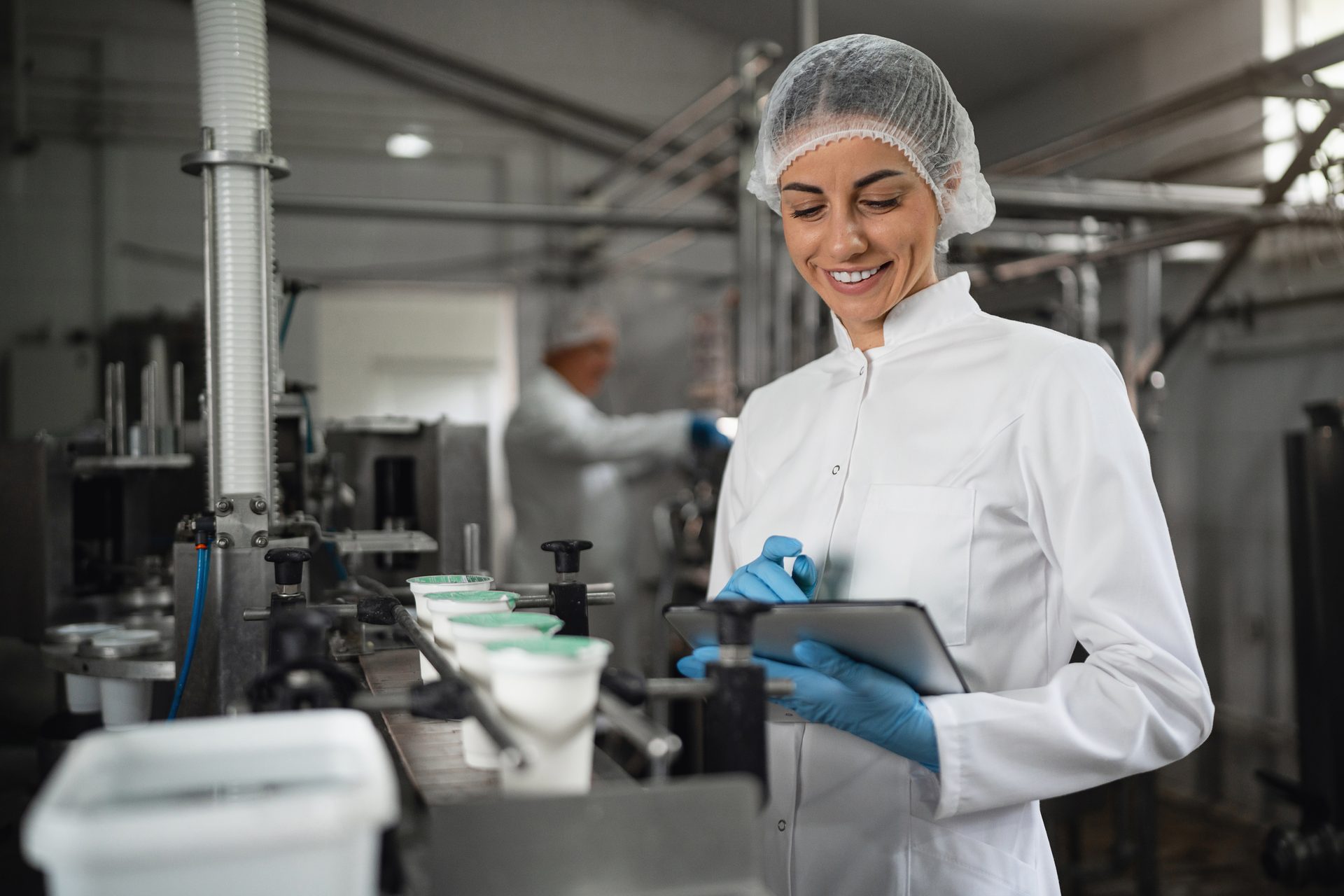Woman in cleanroom attire inspecting a food production line with a tablet.