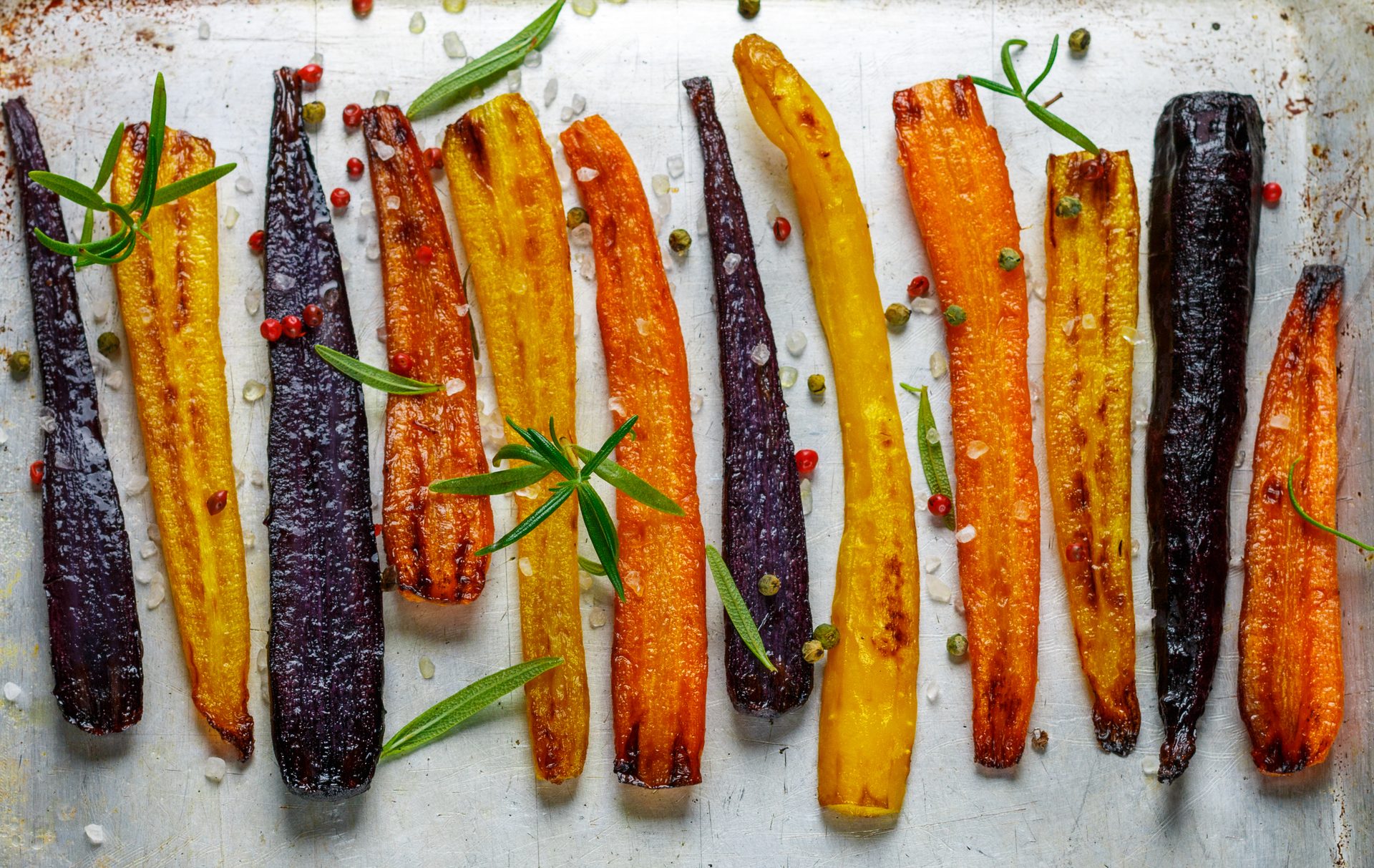 Roasted multi-colored carrots with herbs and spices on a tray.
