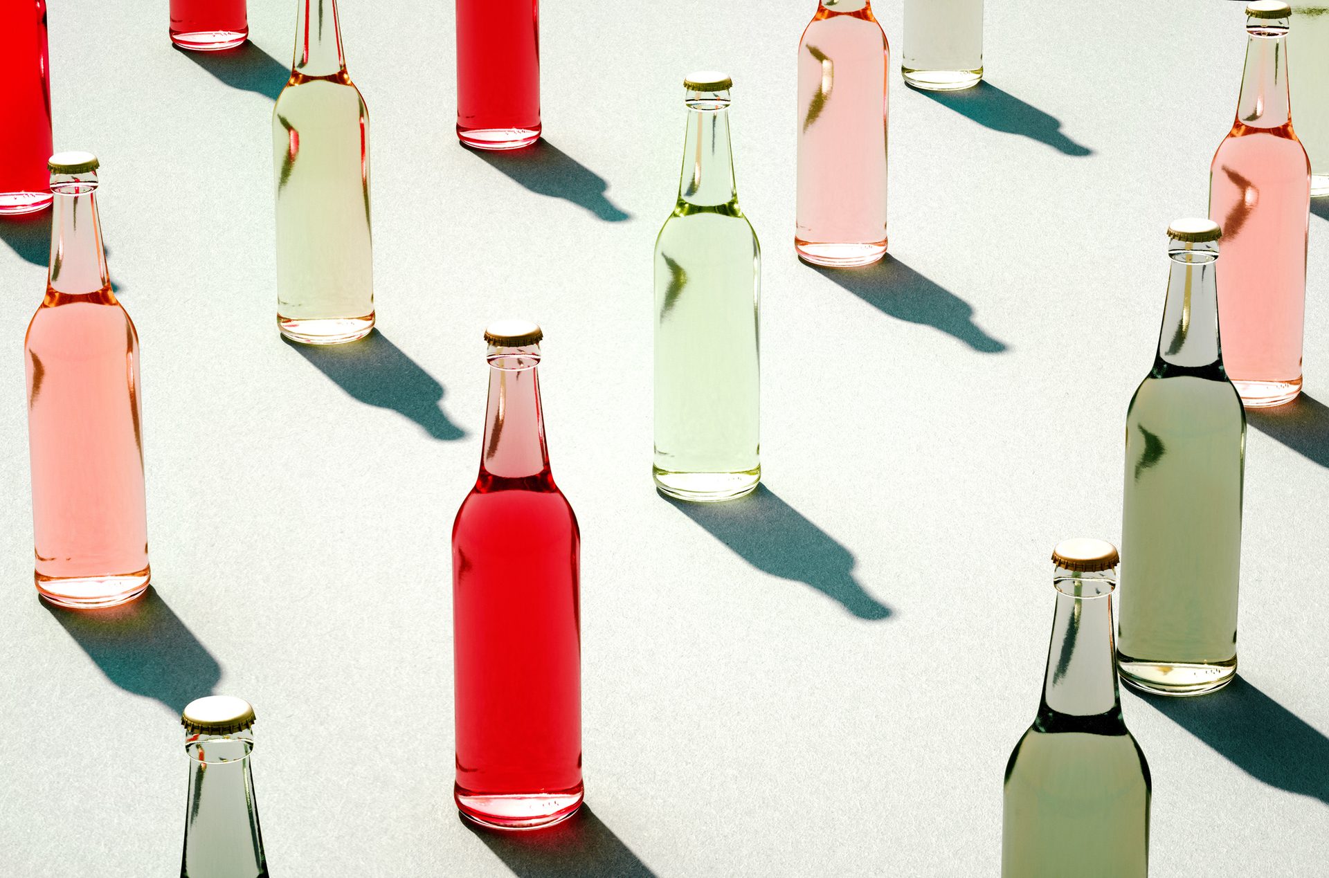 A vibrant arrangement of glass bottles filled with red, pink, and light green beverages on a bright surface.