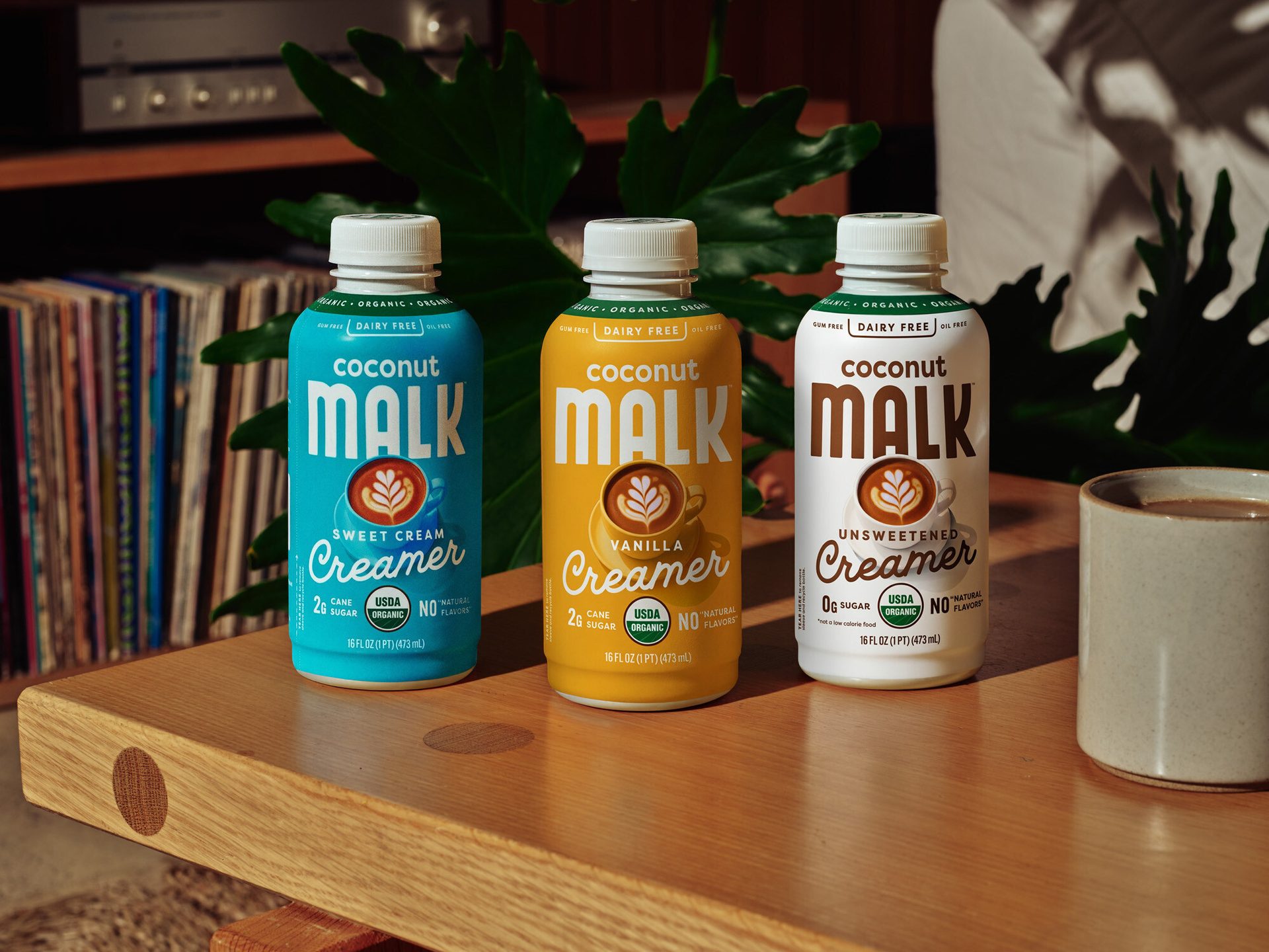 Three Coconut Malk creamers (Sweet Cream, Vanilla, Unsweetened) on a wooden table.