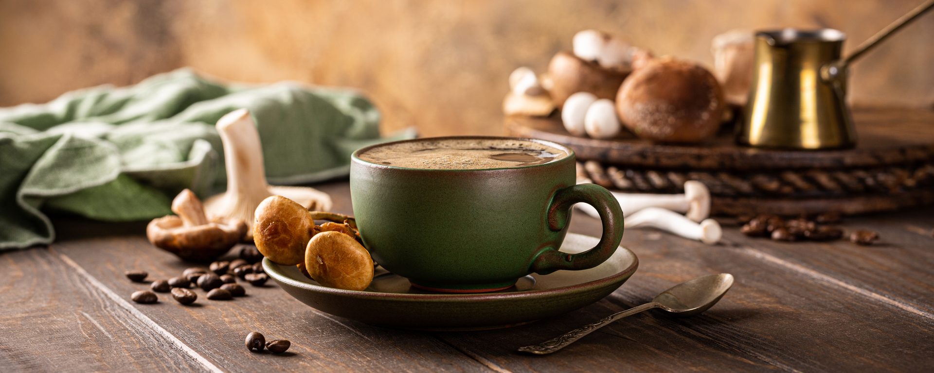 Green coffee cup surrounded by various mushrooms and coffee beans on a rustic wooden table.