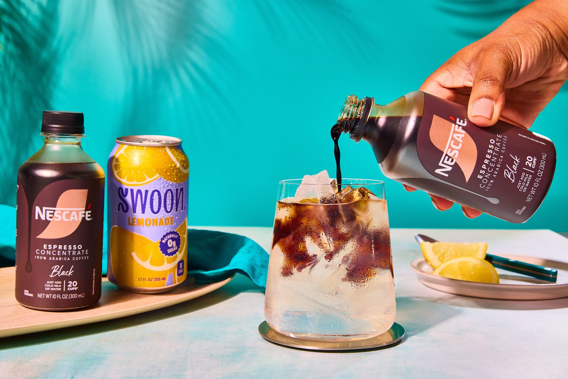 Hand pours Nescafe espresso concentrate into iced lemonade. Nescafe bottle & Swoon lemonade can.