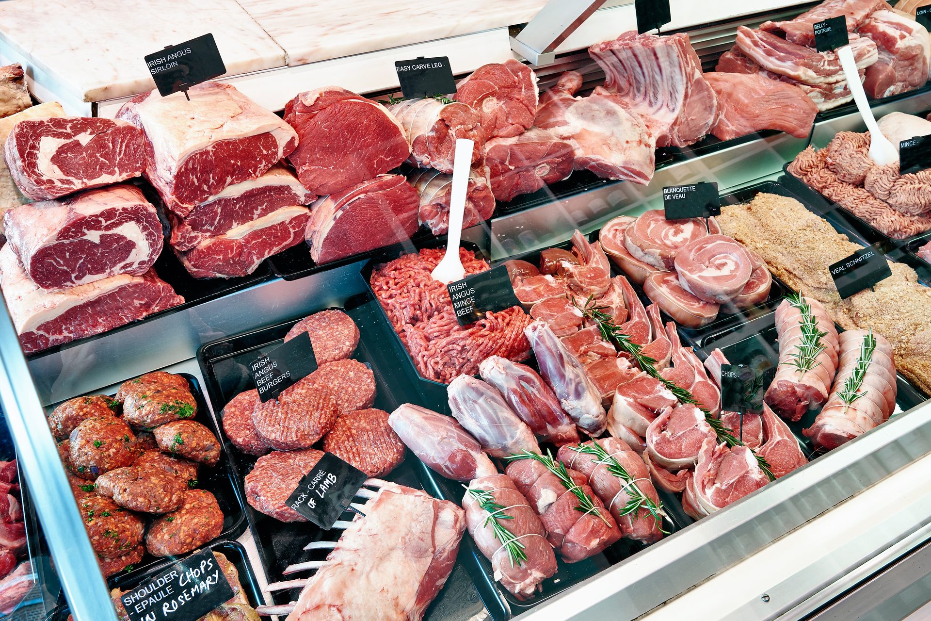 A butcher's display case filled with assorted raw meats, including beef, lamb, and veal cuts, burgers, and mince.