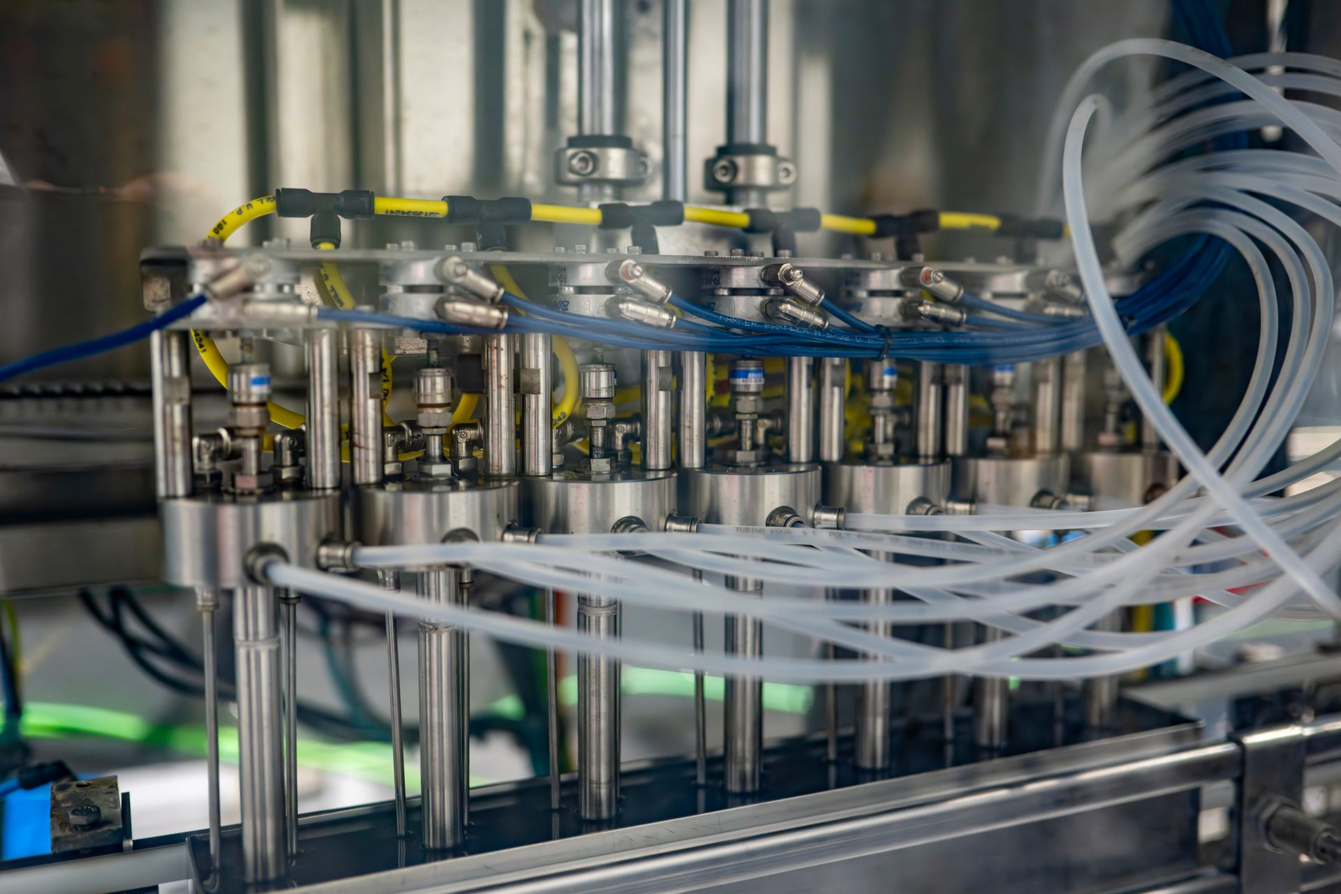 Close-up of an industrial filling machine with multiple stainless steel nozzles, intricate wiring, and tubes.
