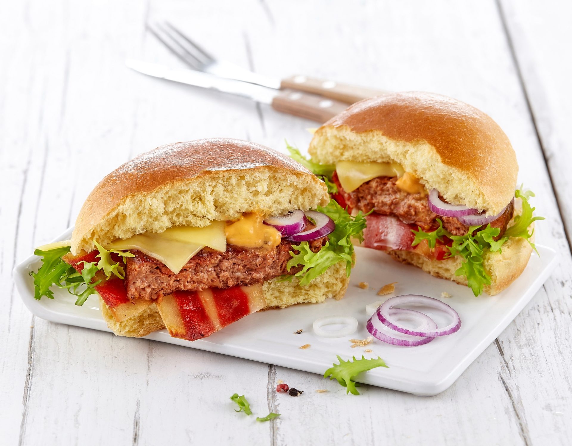 Two gourmet burgers cut in half on a white plate, showing patty, bacon, cheese, lettuce, and onion.