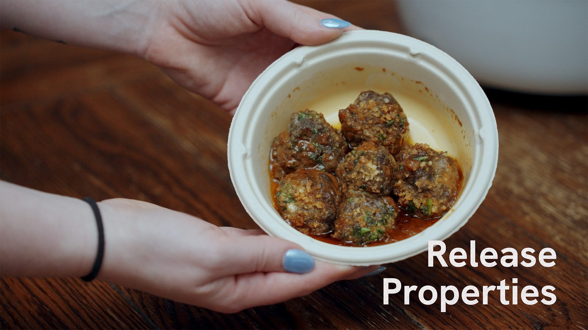 Hands holding a bowl of seasoned meatballs in sauce.