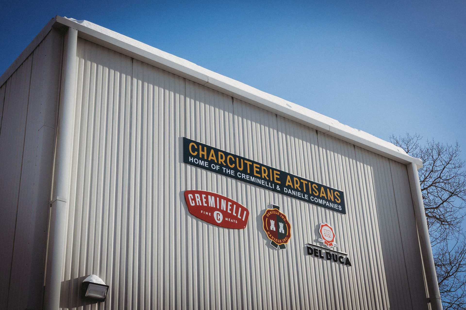 Exterior view of the Charcuterie Artisans building, featuring signs for Creminelli, Daniele, and Del Duca.