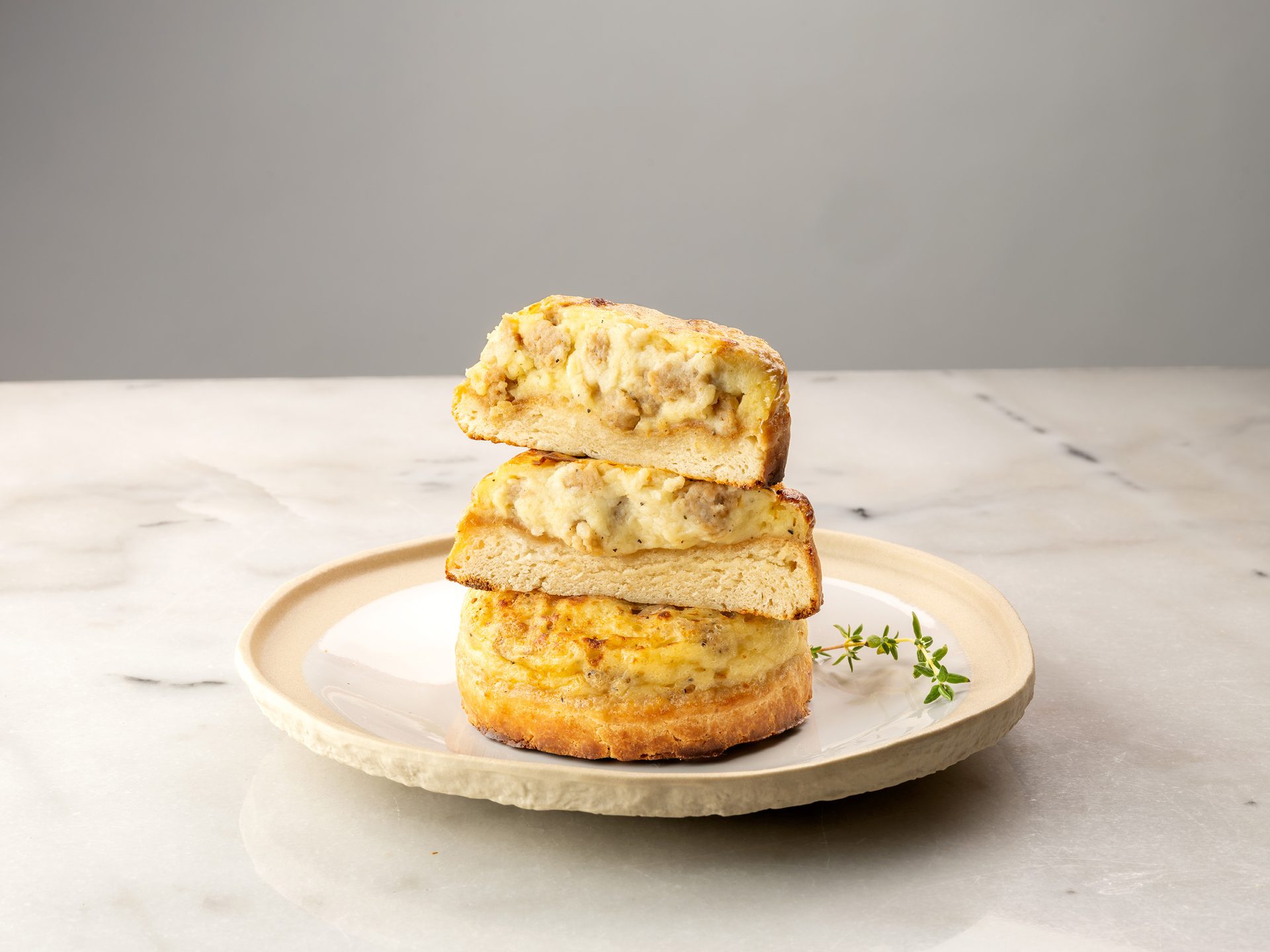 Stacked savory bread slices with sausage and cheese filling on a plate with thyme.