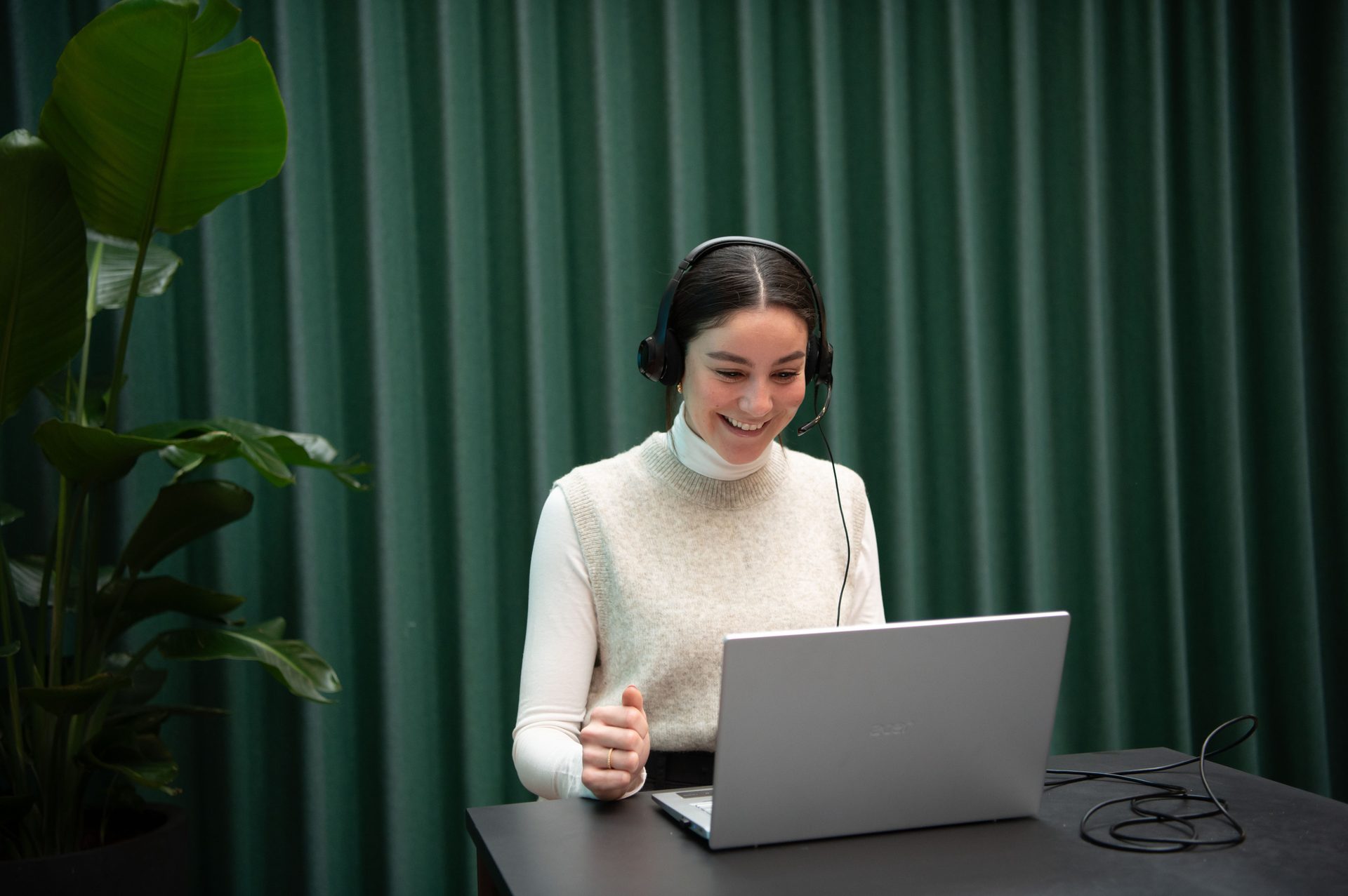 Smiling woman with a headset, sitting in front of a laptop. 