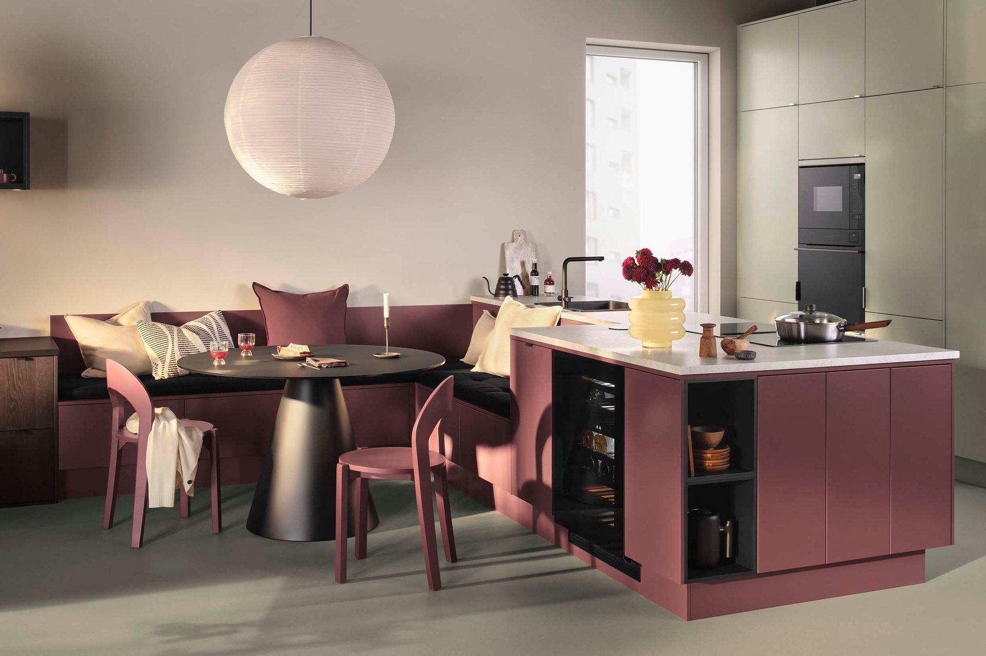 Modern kitchen and dining area with burgundy and sage cabinetry, built-in seating, and paper lantern.