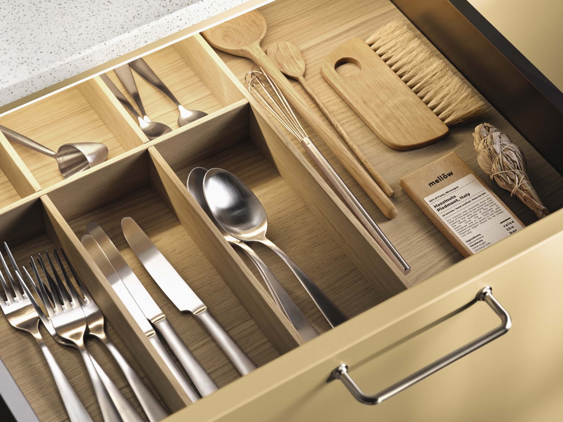 Organized kitchen drawer with wooden dividers, holding cutlery, cooking tools, chocolate, and sage.