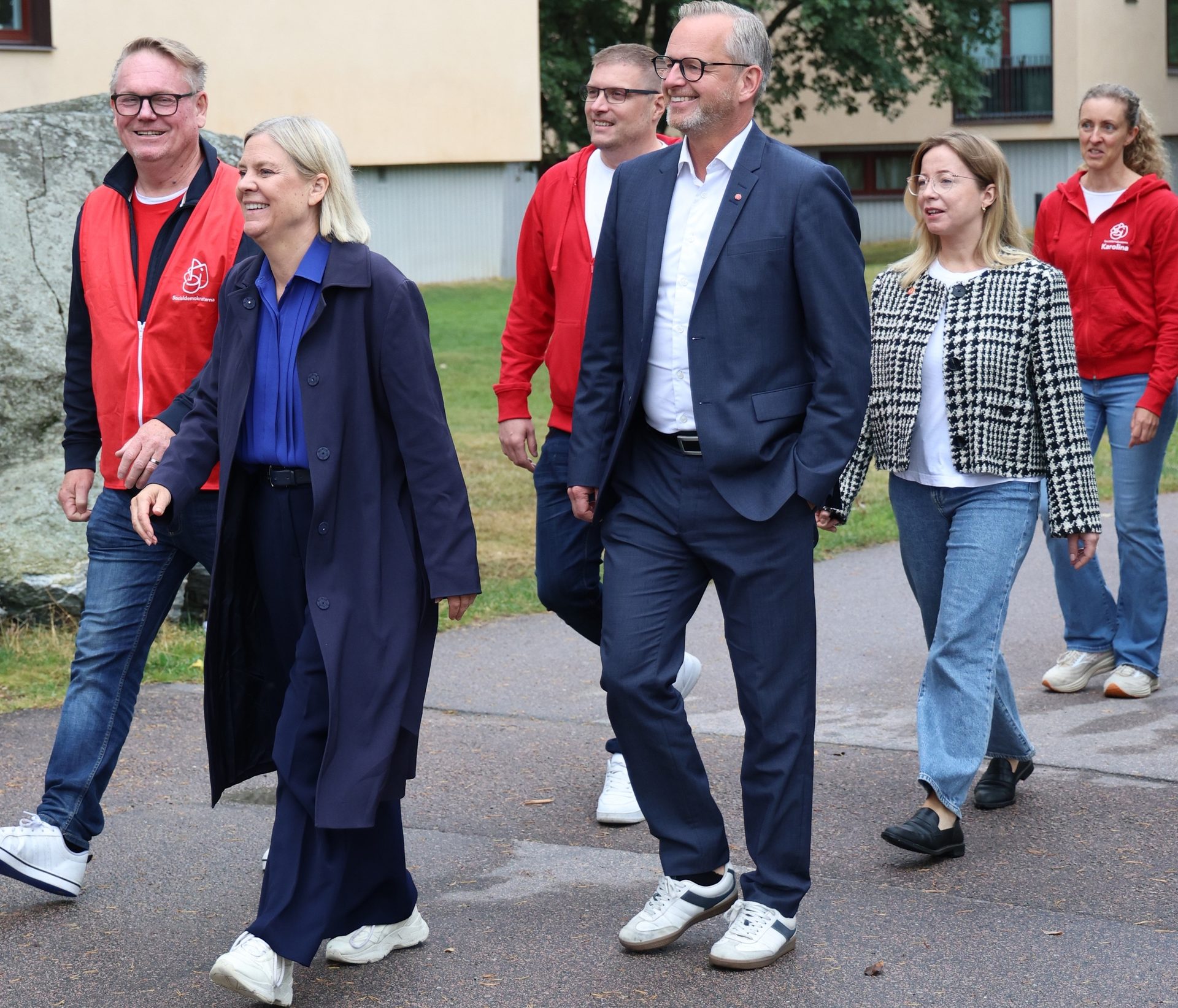 Group of six people, including a woman in a blue coat, walking outdoors on a paved path.