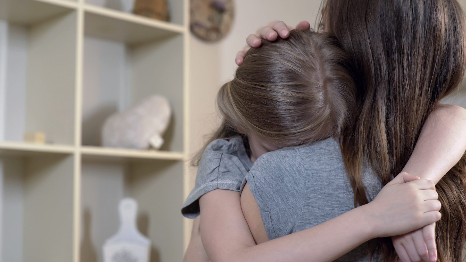 Two girls embrace, one comforting the other, showcasing sisterly love and support.