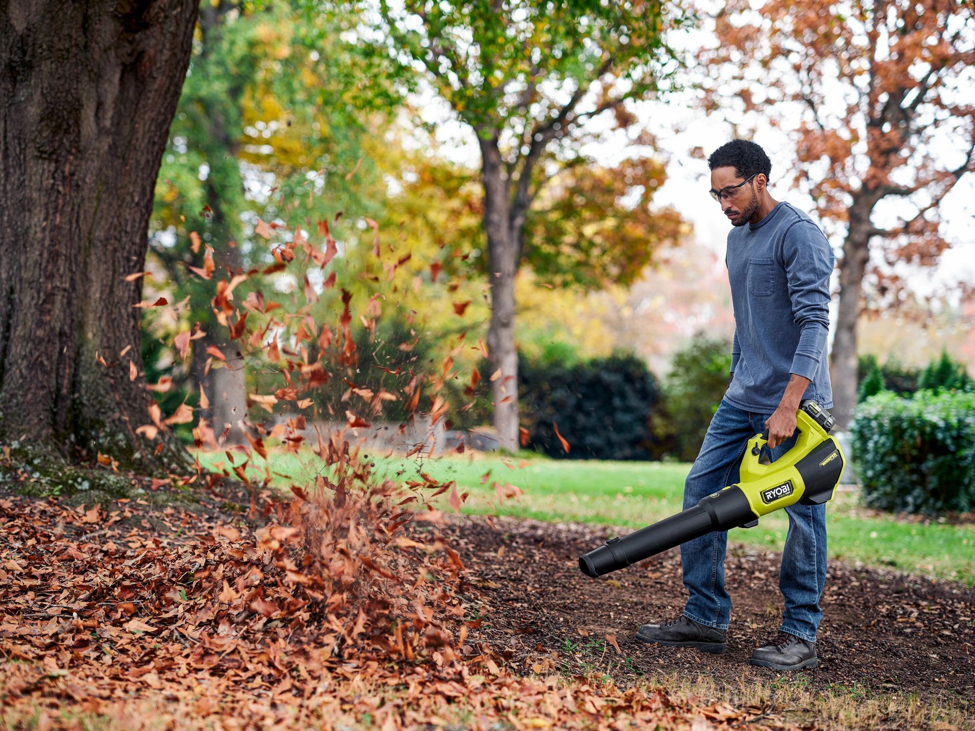 Man blows autumn leaves with a green Ryobi leaf blower.