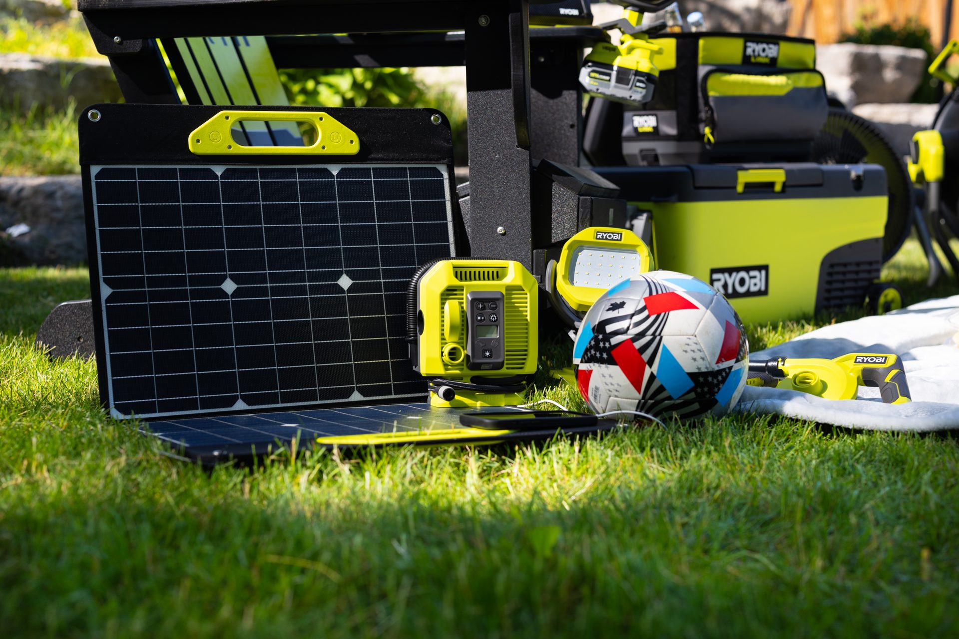 Ryobi solar power kit, portable tools, and soccer ball on green grass.