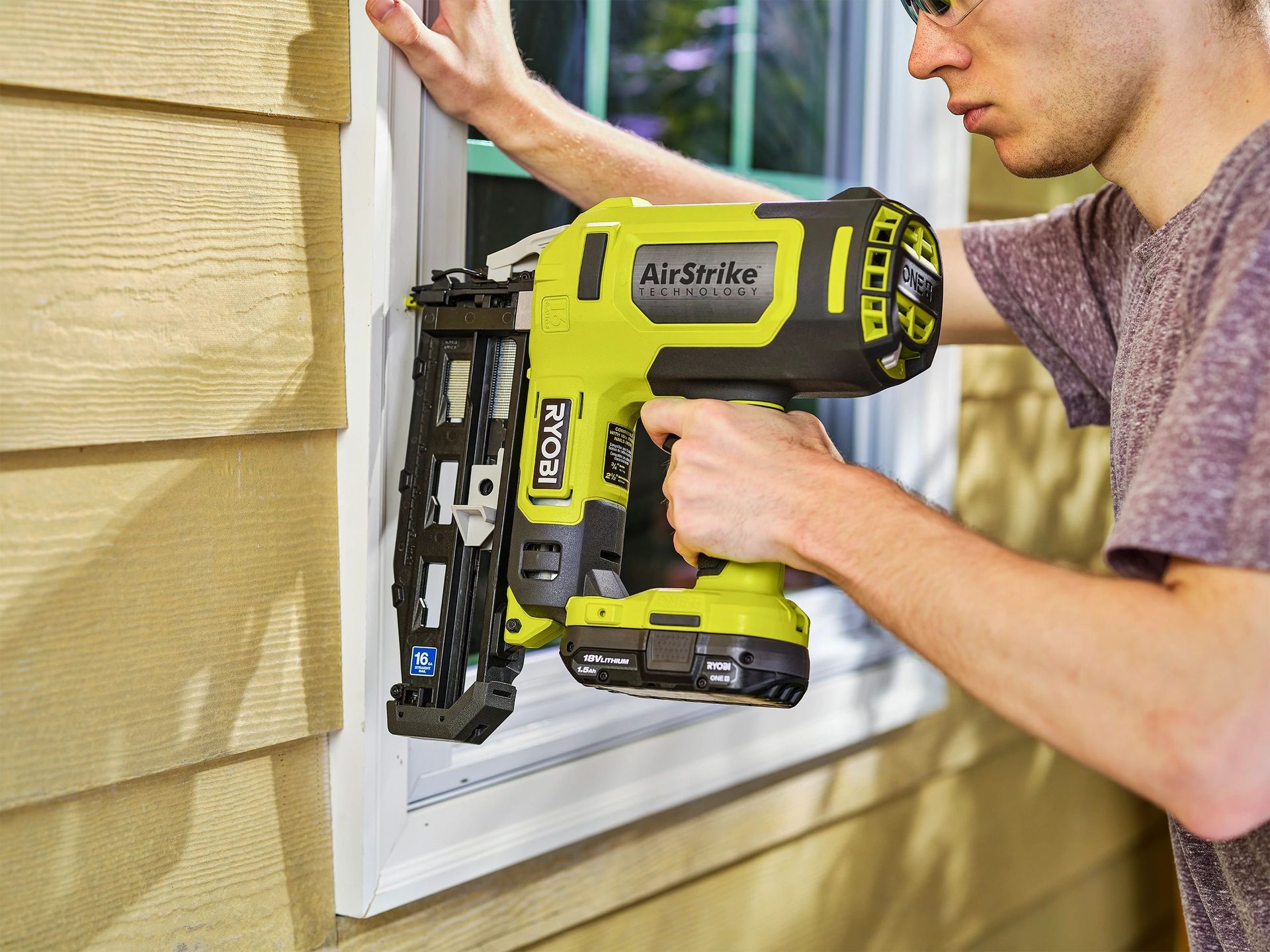 Person using a Ryobi AirStrike nail gun on house siding by a window.