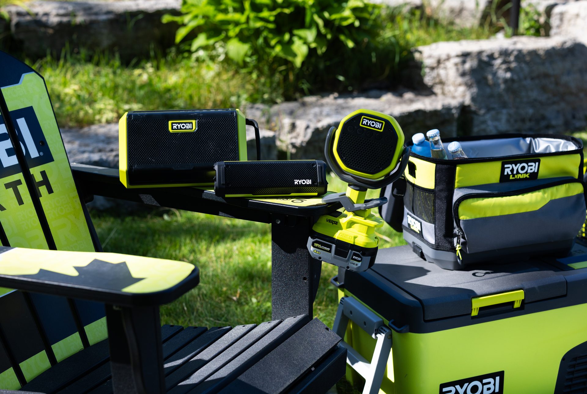 Ryobi branded outdoor leisure setup with a chair, speakers, and cooler on a lawn.