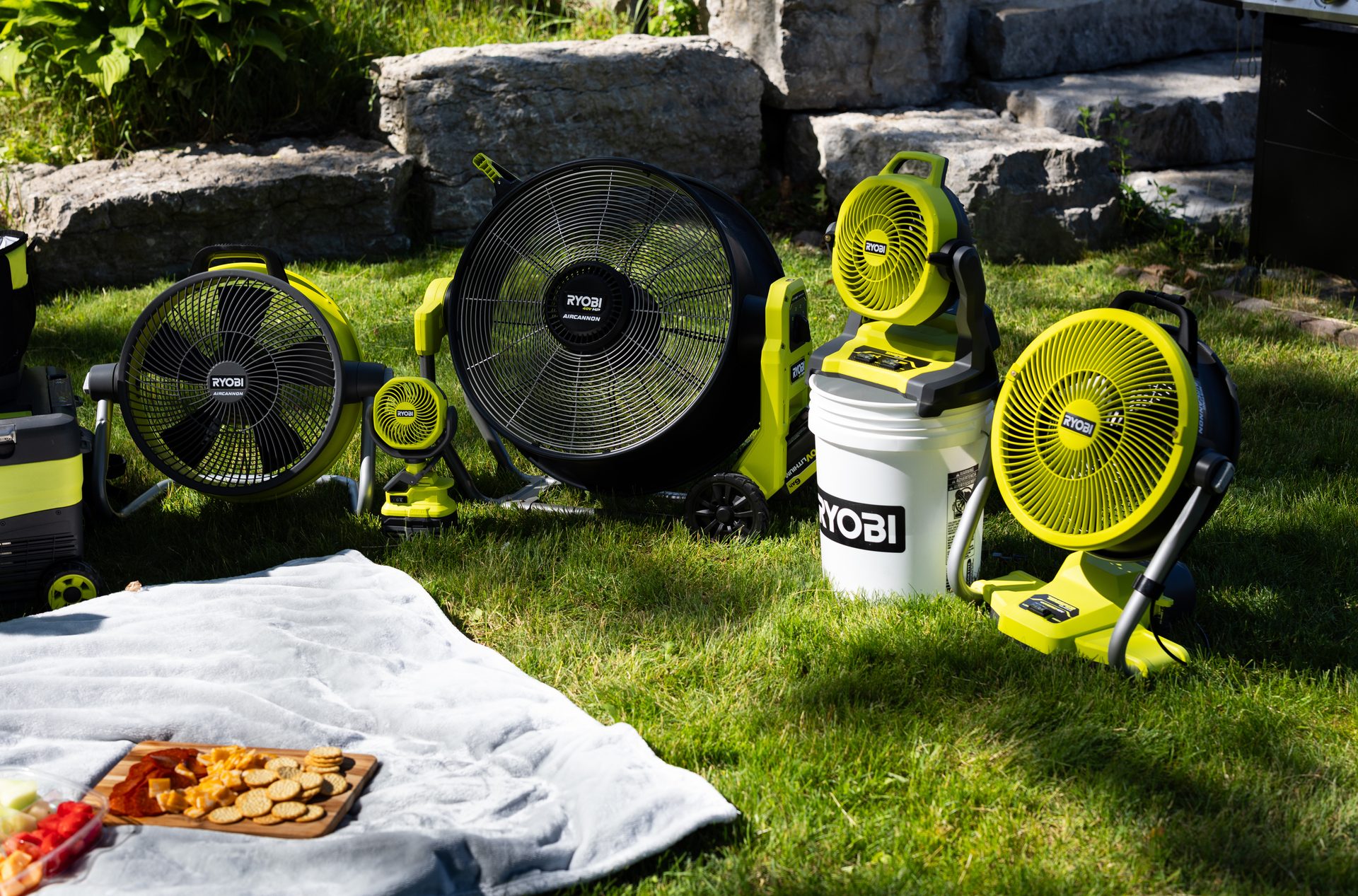 Ryobi fans, mostly lime green and black, arranged outdoors on grass with a picnic blanket and snacks.