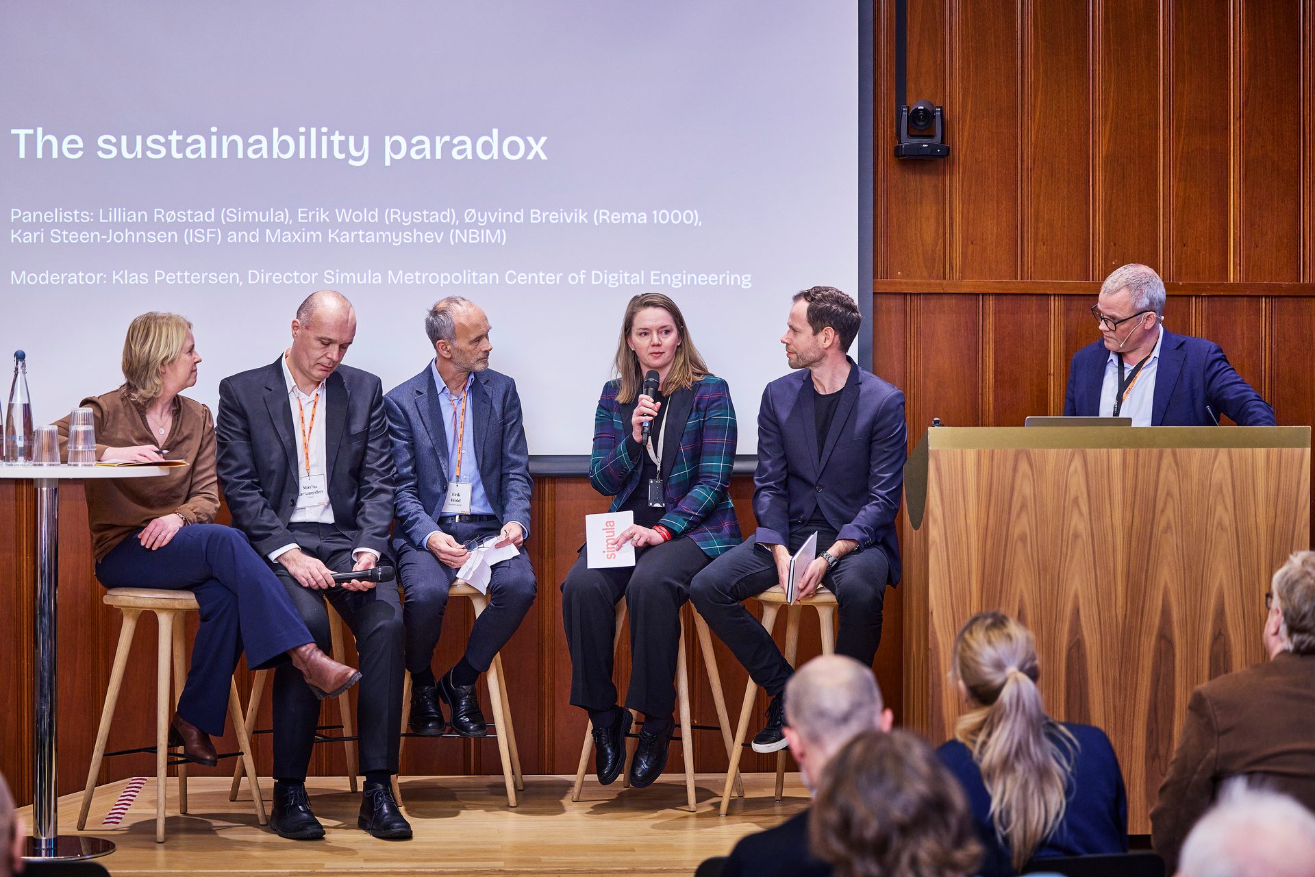A panel discusses "The sustainability paradox" at a conference.