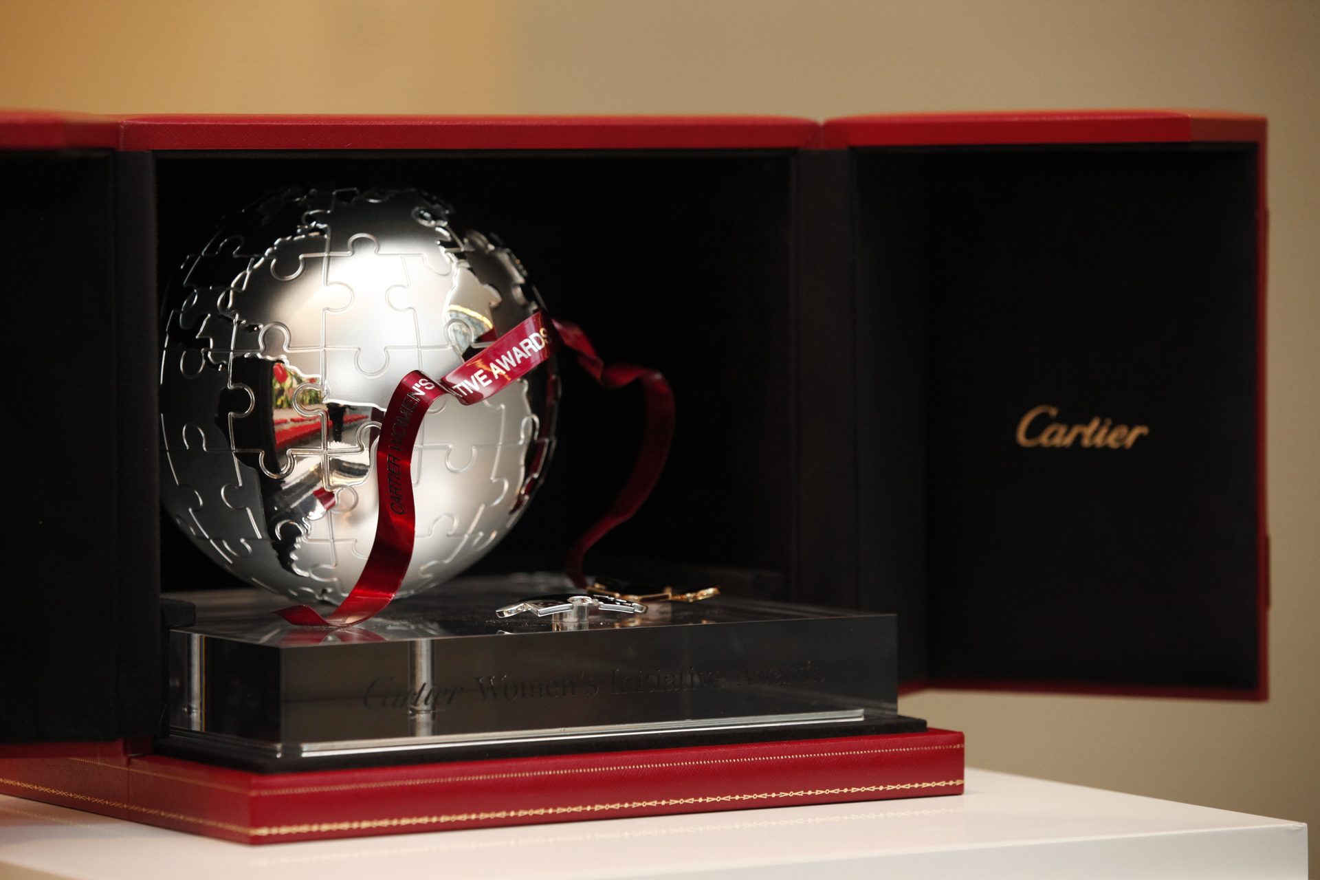 Silver puzzle-piece globe trophy with a red "Cartier Women's Initiative Awards" ribbon in a Cartier box.