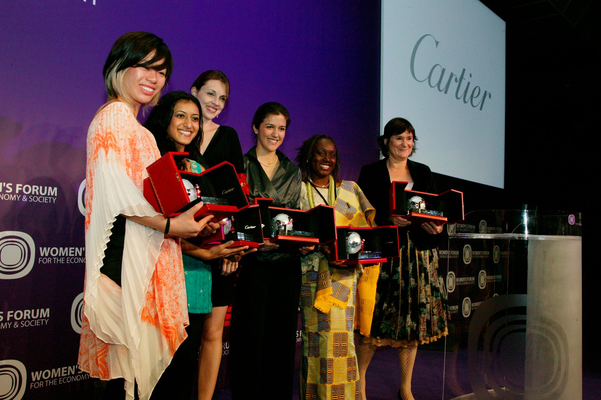 Six smiling women on stage receive awards in red Cartier boxes at the Women's Forum.
