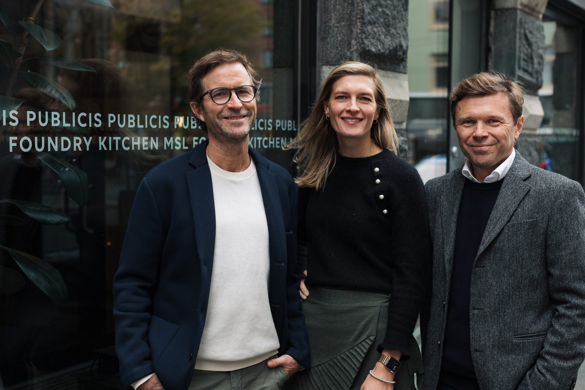 Three smiling professionals, two men and one woman, stand in front of a Publicis building.
