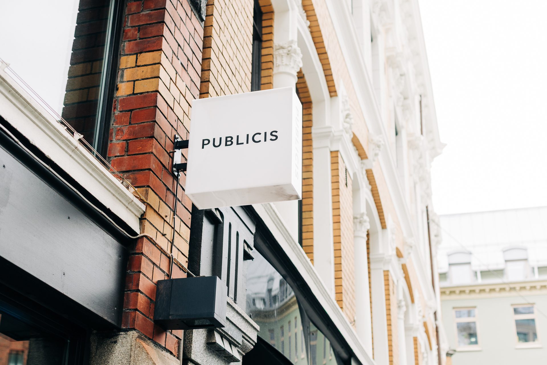 A white square sign displaying "PUBLICIS" on a brick building with decorative columns.