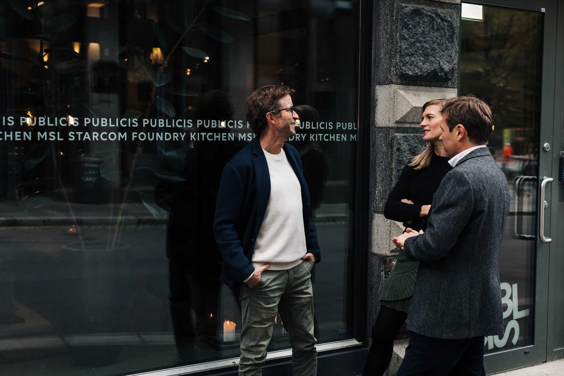 Three people chatting in front of a window displaying "PUBLICIS" text.